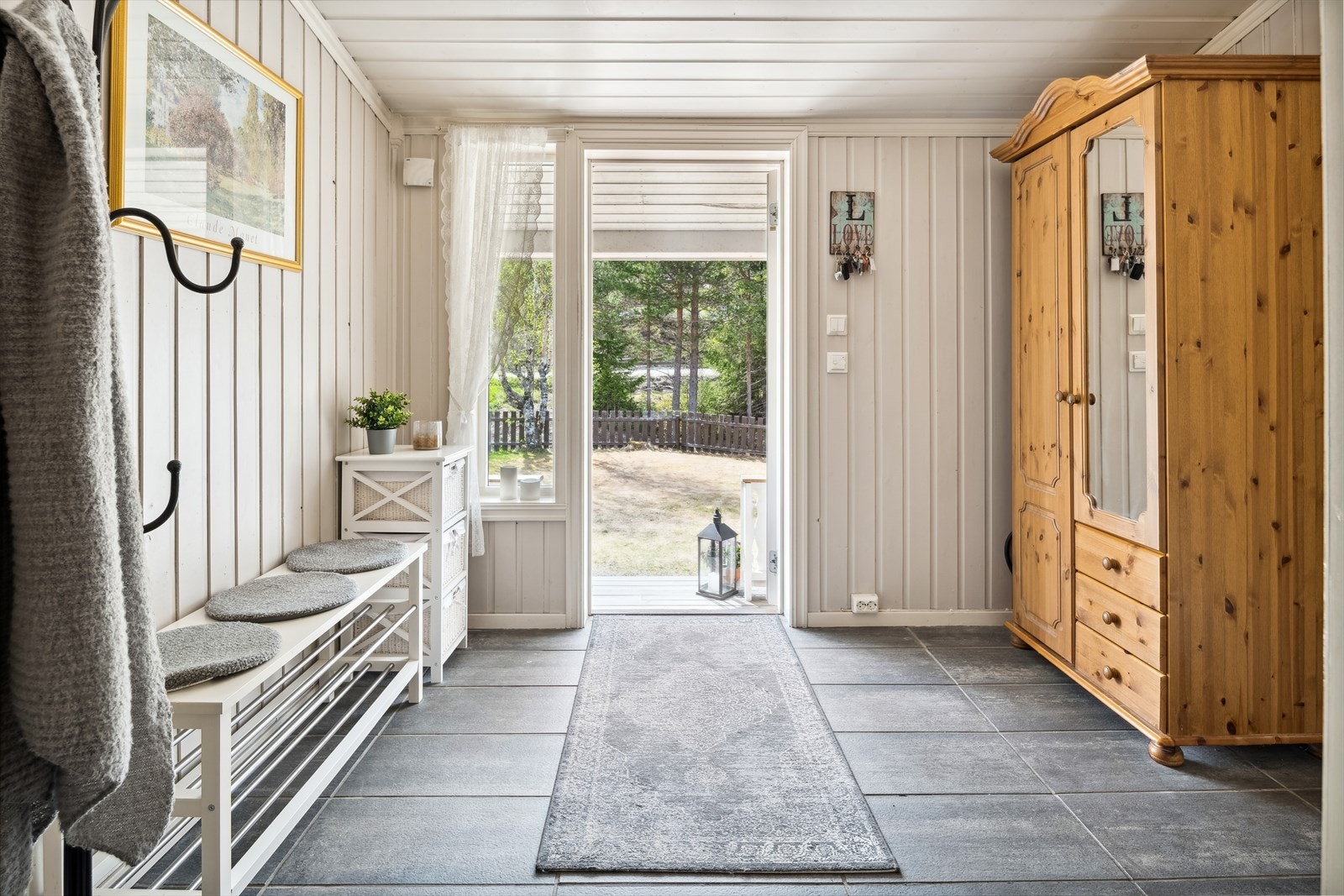 Du ønskes velkommen inn i en lys og romslig entré med mørke fliser på gulv med gulvvarme og lysmalt trepanel på veggene. God oppbevaringsplass i medfølgende garderobeskap, samt adkomst til en praktisk bod. Galleribilde