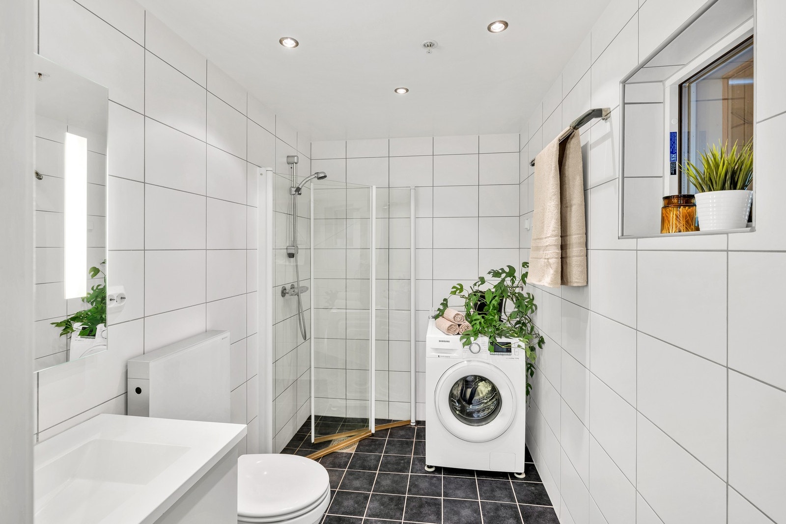 Lyst og flislagt bad på ca. 5kvm. Badet er utstyrt med en praktisk innfellbar dusjnisje, toalett, opplegg for vaskemaskin og et praktisk luftevindu. Galleribilde