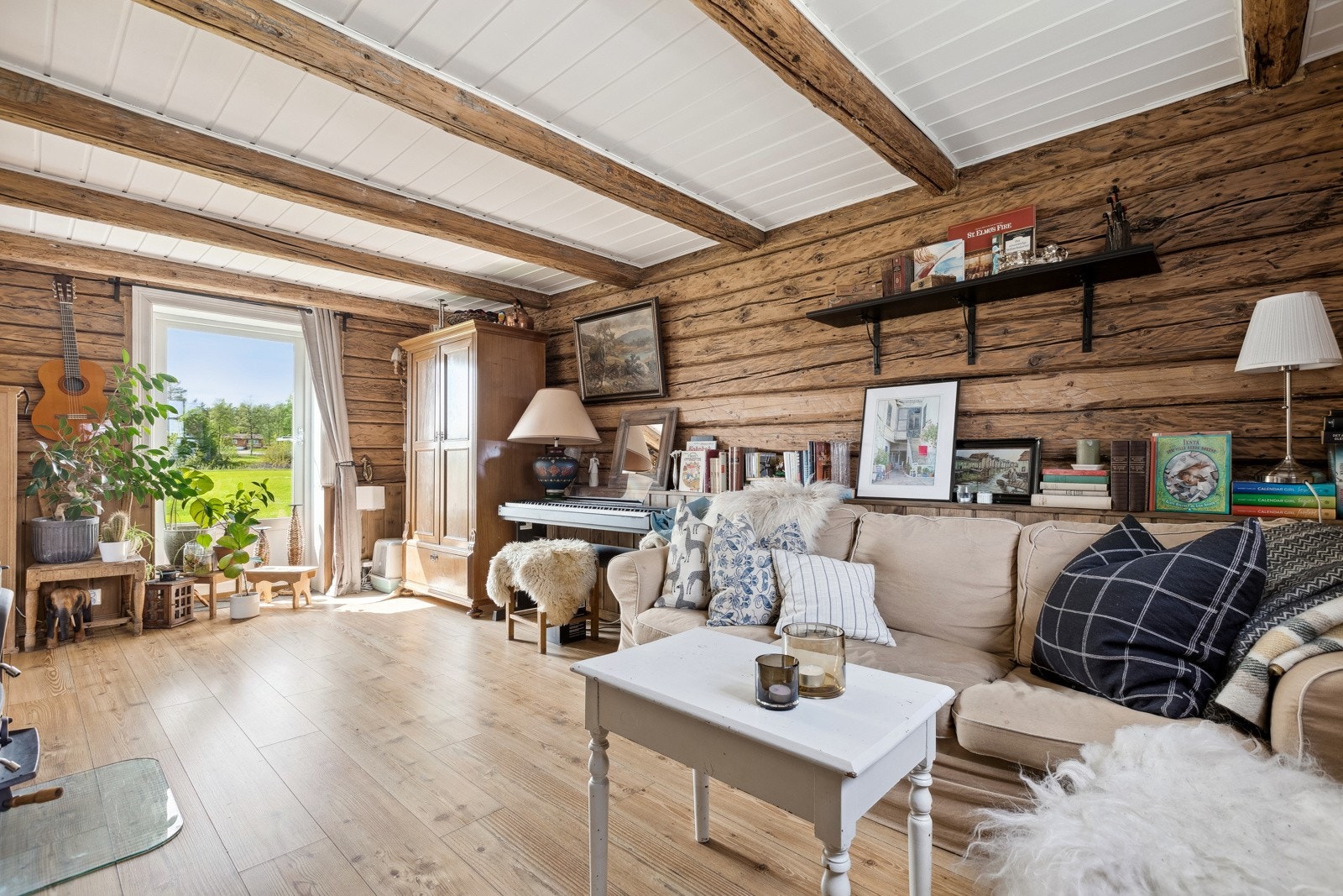 Koslig stue i kårboligen med tømmervegger og lyse tak. Det er plass for sofamøblement og spisebord. Galleribilde