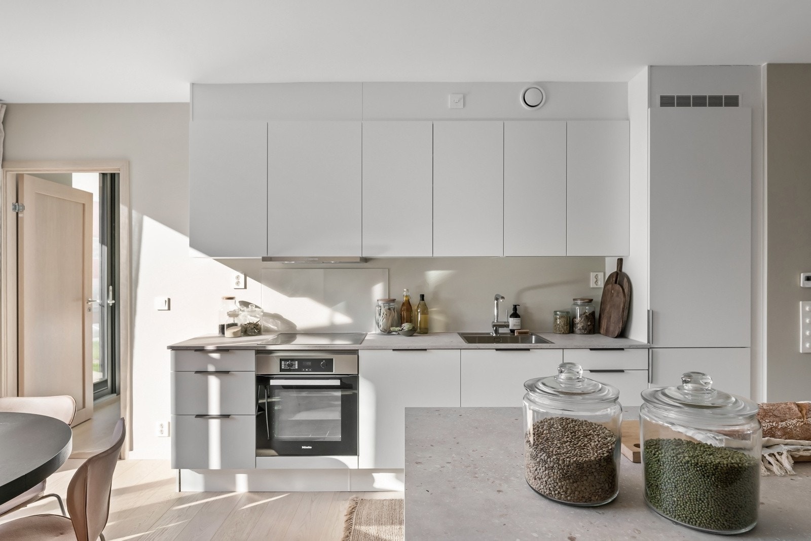 Innredningens rene linjer passer godt inn i leilighetens stilmessige uttrykk og fremstår samtidig som svært funksjonell med hvite, glatte fronter med soft close, benkeplate i lys laminat og nedfelt oppvaskkum i stål. Galleribilde