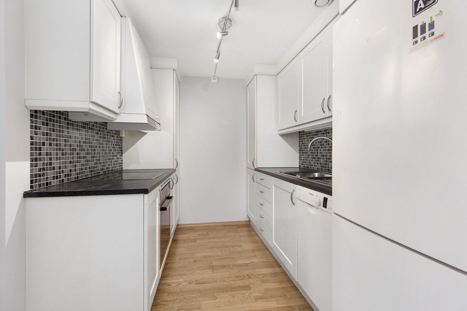 Lyst og moderne kjøkken med profilerte fronter, laminat benkeplate og fliser under overskap. Galleribilde