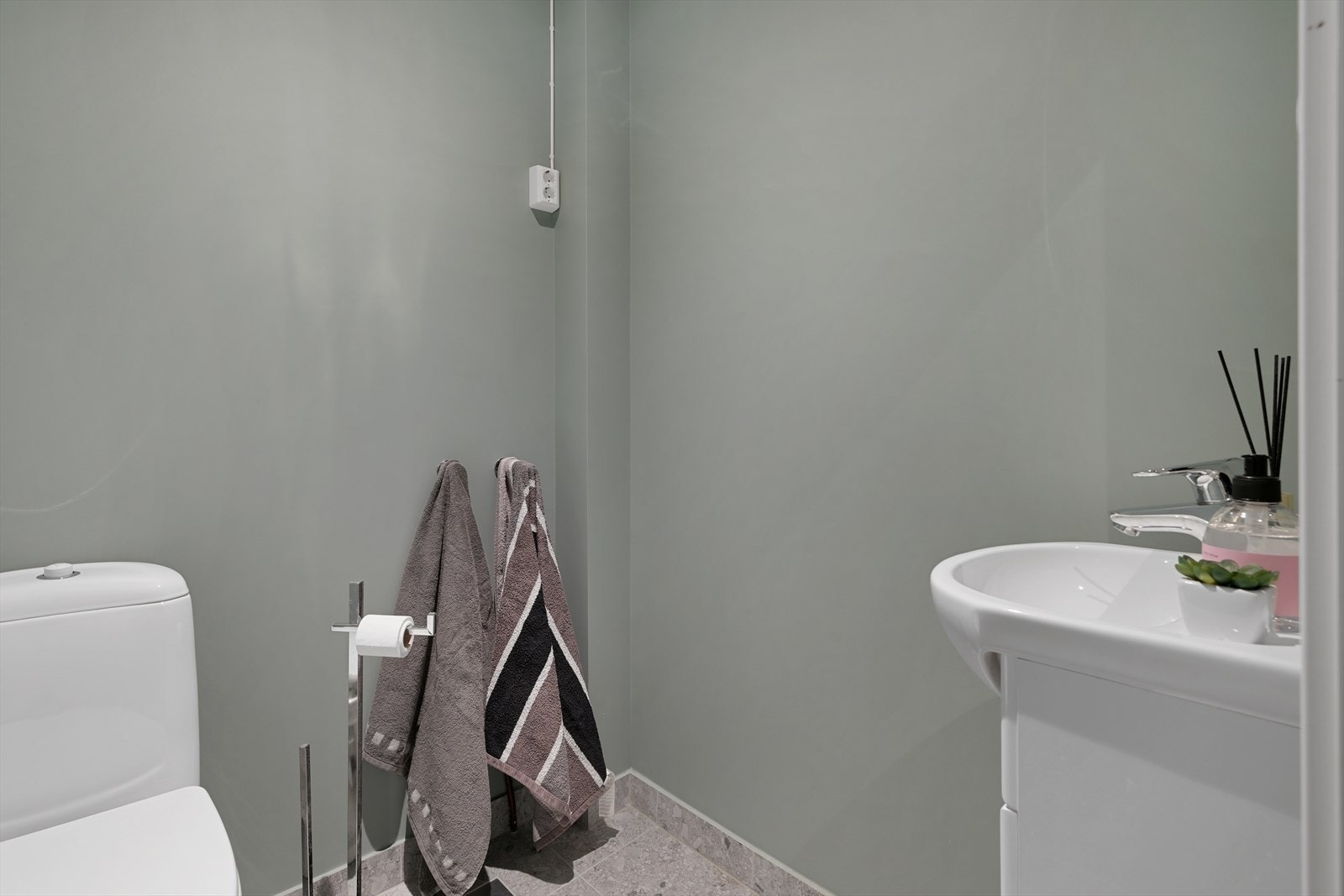Gjestetoalett med fliselagt gulv og servant, med opplegg for vaskemaskin. Galleribilde