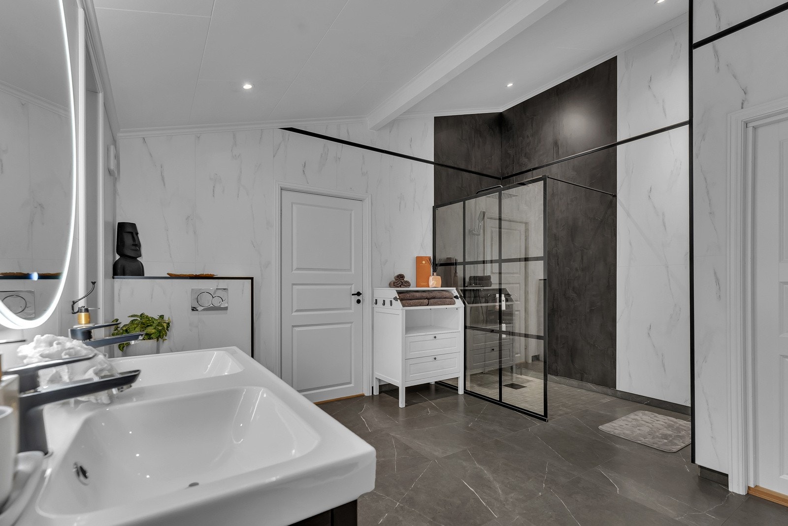 Innredning med dobbel servant med 2 ett-greps armaturer, speil med belysning på vegg, dobbel stikkontakt i innredning, vegghengt toalett, dusjnisje med glassvegg og ett-greps armatur med dusjhode samt hånddusj. Galleribilde