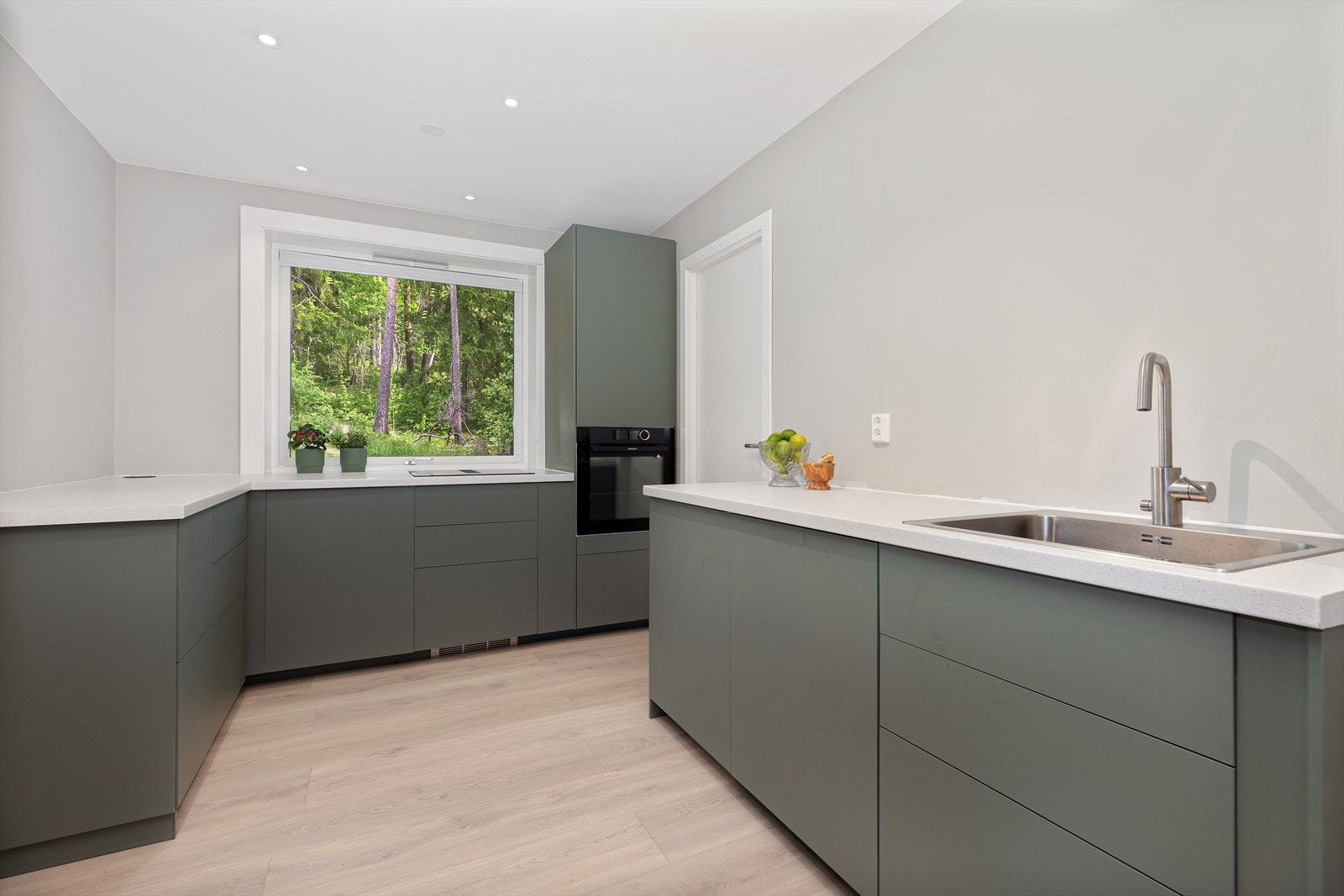 Lekkert kjøkken fra 2023 med downlights i tak og slette fronter i moderne, tidsriktig grønnfarge, samt benkeplate av laminat. Galleribilde