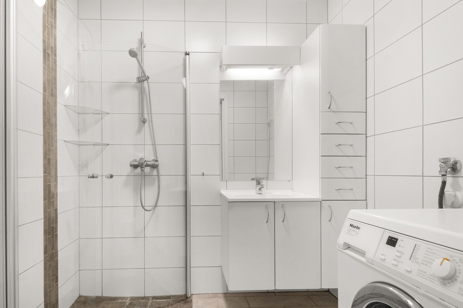 Bad - Flislagt bad med dusjnisje med dusjvegg, vegg hengt toalett, servant med skap speil og opplegg for vaskemaskin. Varmekabler i gulv. Galleribilde