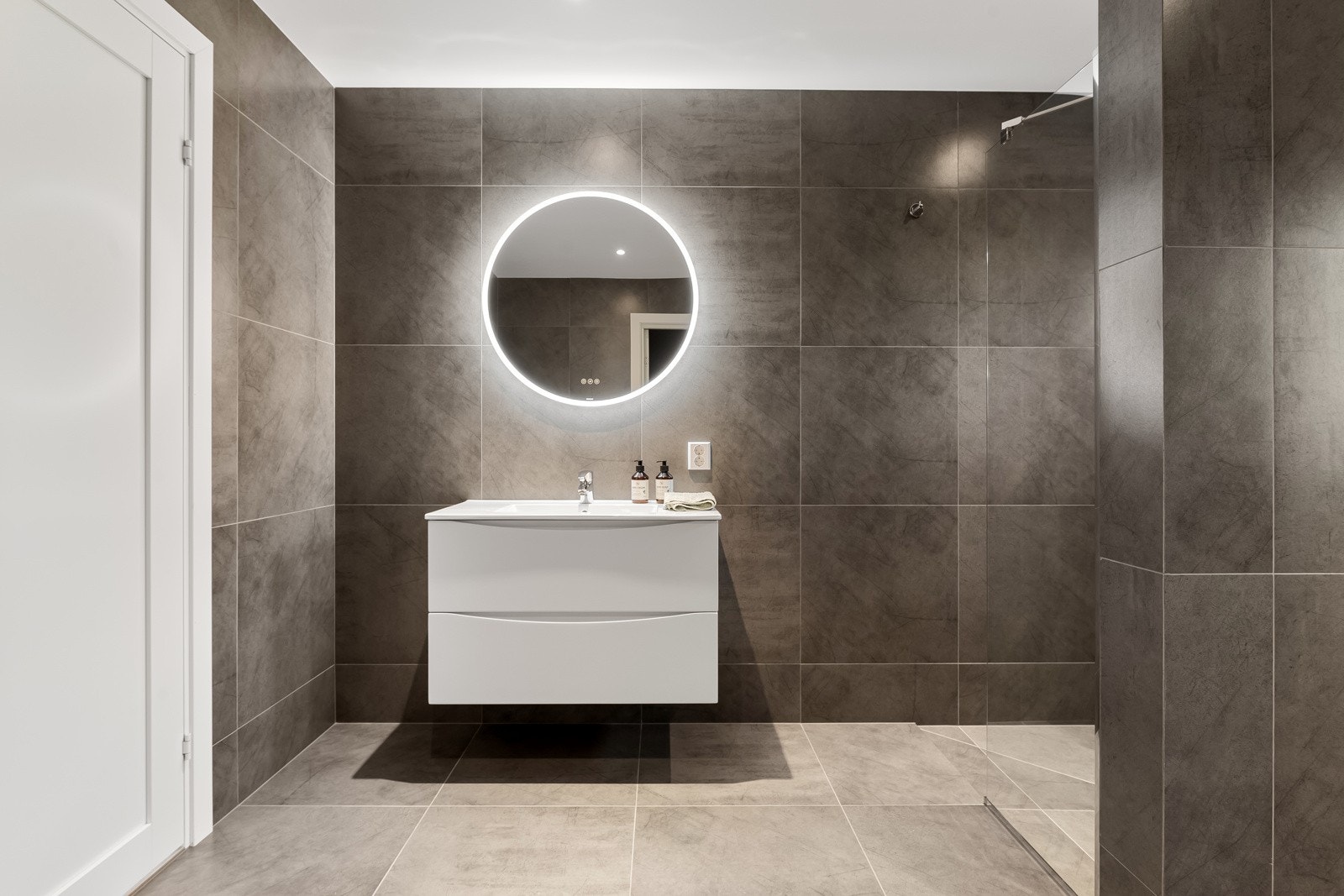 Tiltalende bad med dusjhjørne, servantskap og vegghengt toalett. Galleribilde