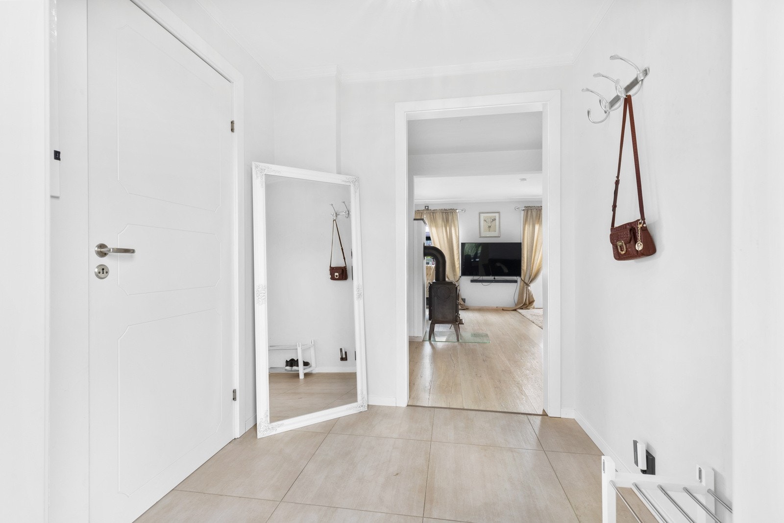 Entreen har store fliser på gulv med varmekabler, lysegrå veggflater og naturlig plass til knagger på veggen. Galleribilde