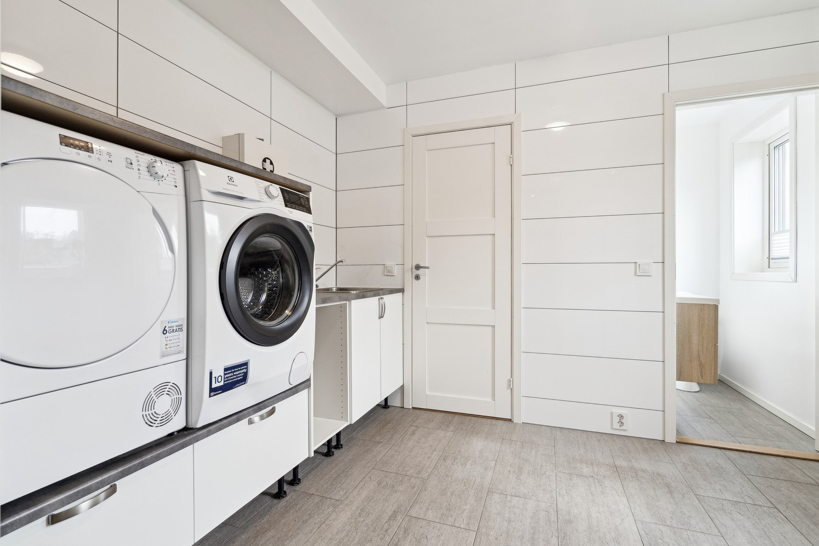 Vaskerom med utslagsvask, og vaskemaskin og tørketrommel i praktisk arbeidshøyde Galleribilde