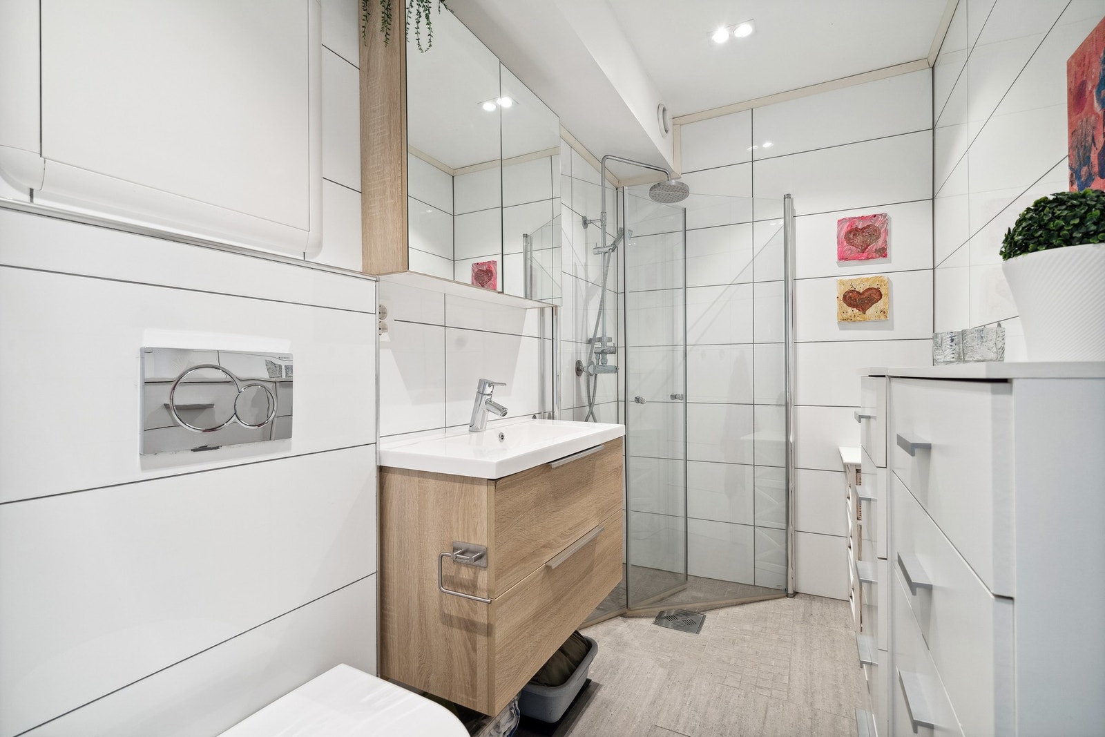 Badet har fliser på gulv, baderomsplater på vegg og moderne bareromsinnredning - dusjhjørne med innsvingbare dører er praktisk og sparer plass Galleribilde