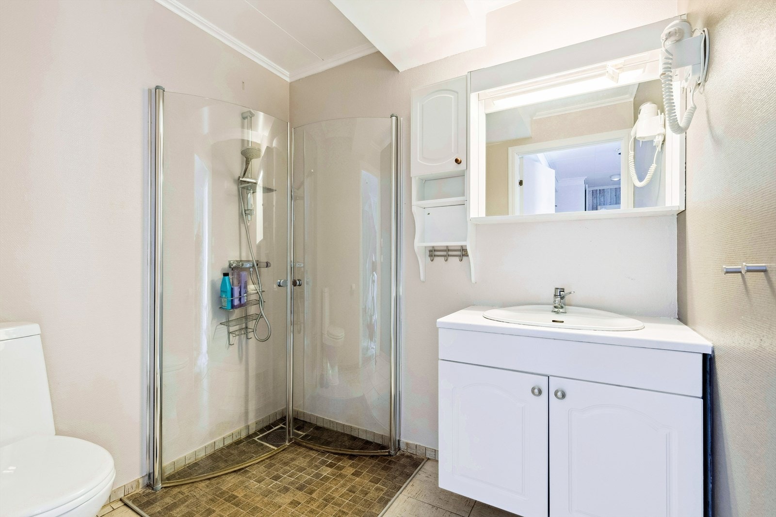 Bad underetasje. Badet har fliser på gulv med varmekabler. Rommet er innredet med en servant innredning og en frittstående wc. Det er dushjørne med glassdører. Det er mekanisk avtrekk. Galleribilde
