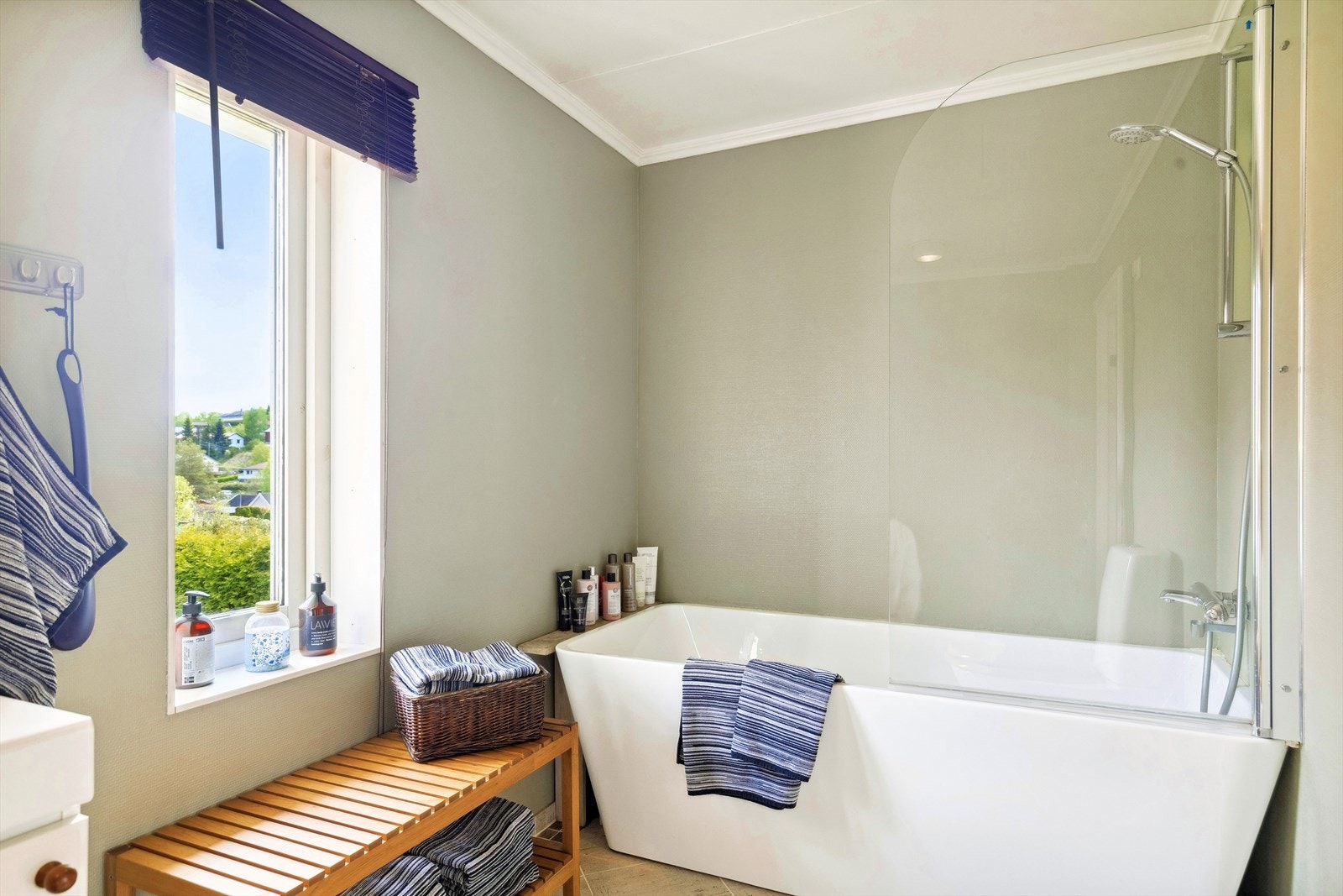 Bad første etasje. Badet har fliser med varmekabel i gulv, malt strie på vegg og himlingsplater i tak. Rommet er innredet med en servant innredning og en frittstående wc. Det er badekar med dusj. Galleribilde
