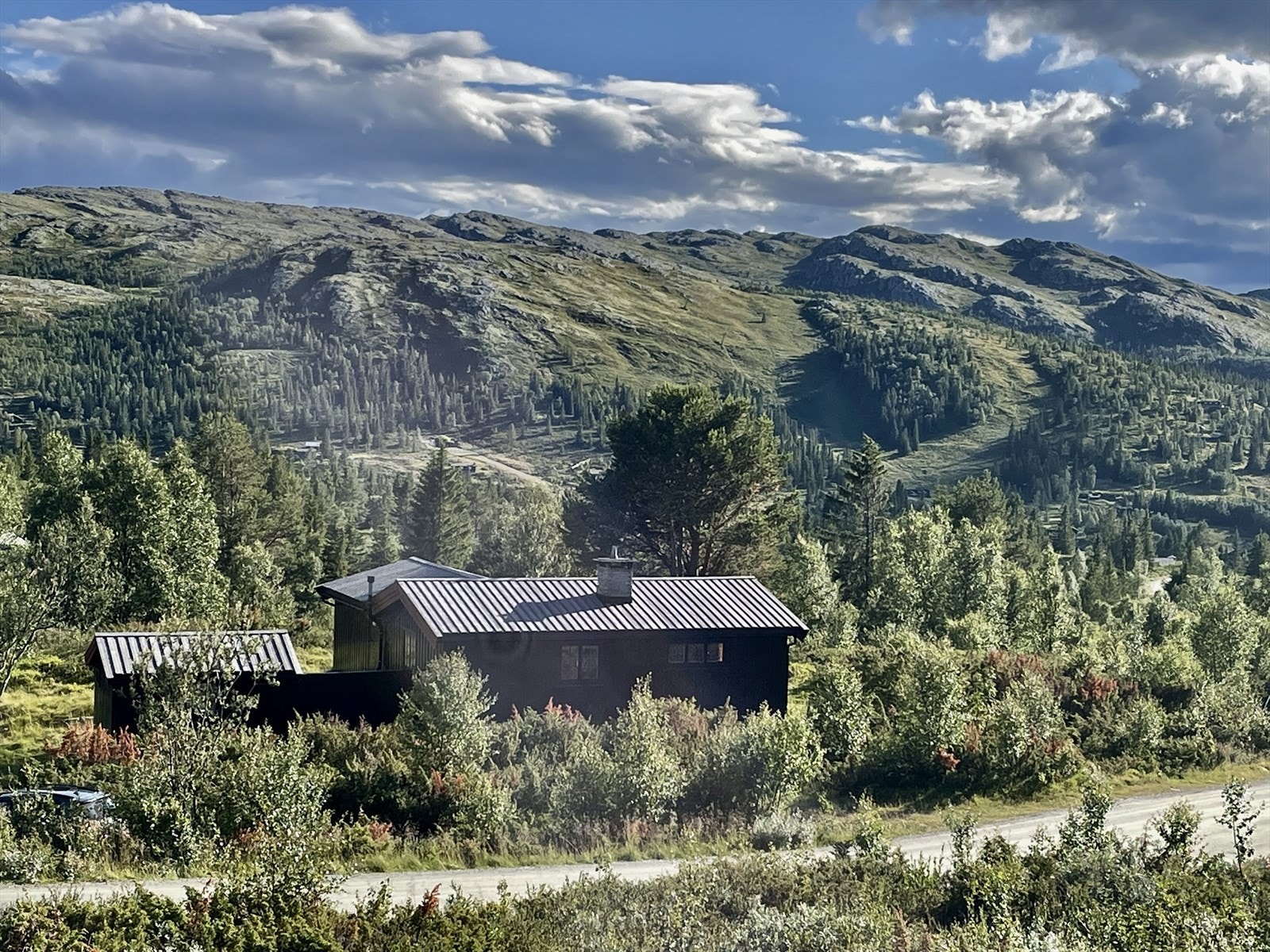Hytta med omkringliggende fjellområder, sett fra litt lengre oppi veien. Galleribilde