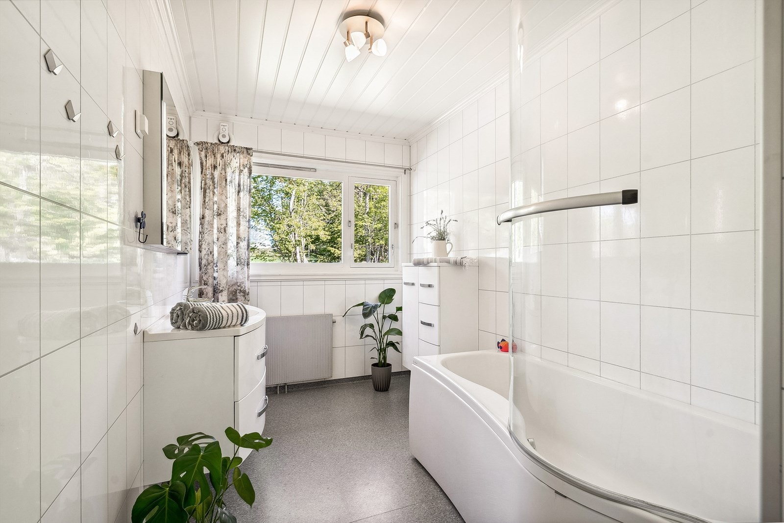 Lyst baderom som er innredet med servant og et praktisk badekar med dusj Galleribilde