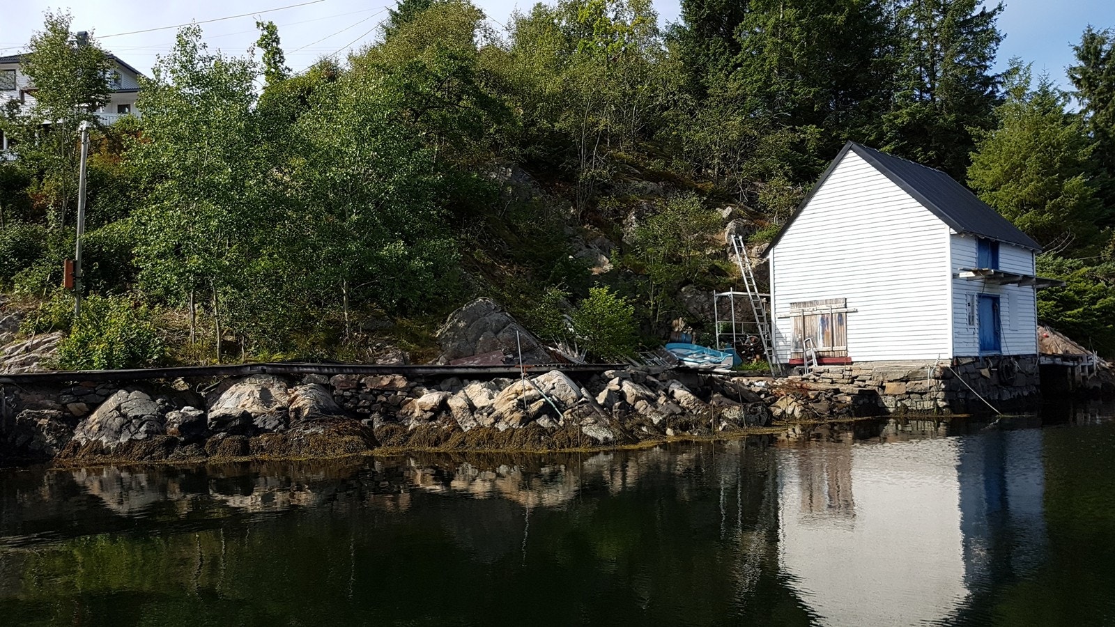 Tomten ligger til venstre for liten blå landstedsbåt. Galleribilde