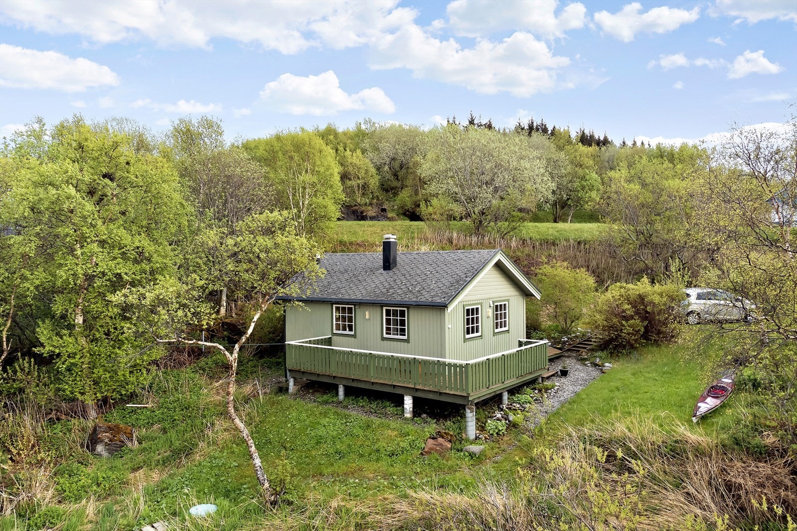 Oversiktsbilde over eiendommen, område rundt er pent opparbeidet og parkeringen ligger like ovenfor hytta. Galleribilde