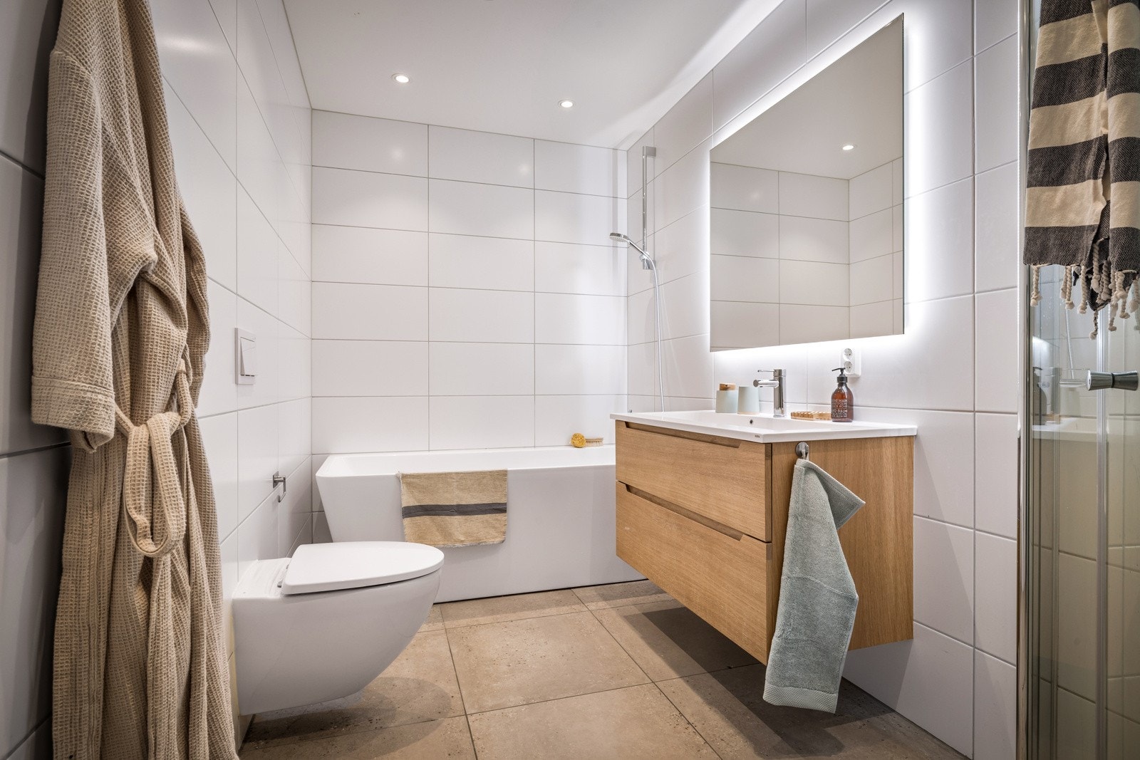 Innfellbart dushjørne i glass til nedsenket dusjsone. Badekar, vegghengt klosett, møblement med servant, dobbel stikkontakt og speil med ledlys. Led-downlights i tak. Galleribilde