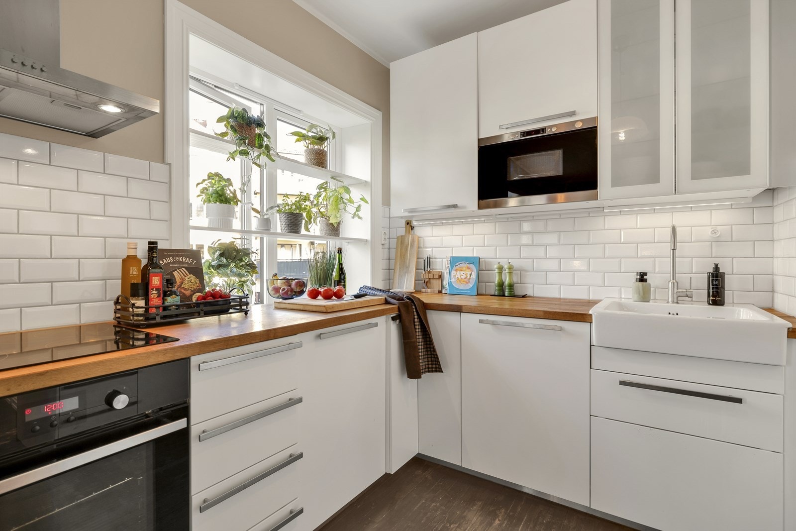 Det er hvite slette fronter, heltre eik/finér benkeplate med nedfelt oppvaskkum, og Subway Tiles fliser mellom overskap og benk Galleribilde