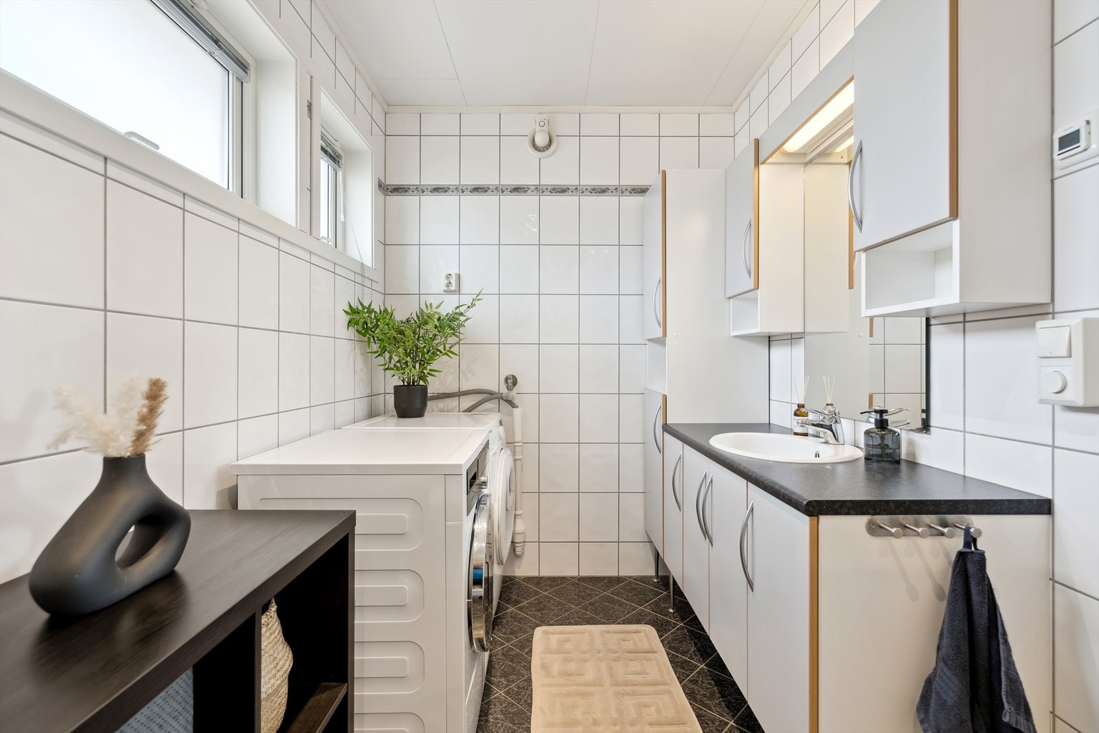 Flislagt baderom med varmekabler i gulv. Rommet er innredet med dusjkabinett, servant over innredning, vegghengt skap med belysning, speil og opplegg til vaskemaskin. Galleribilde