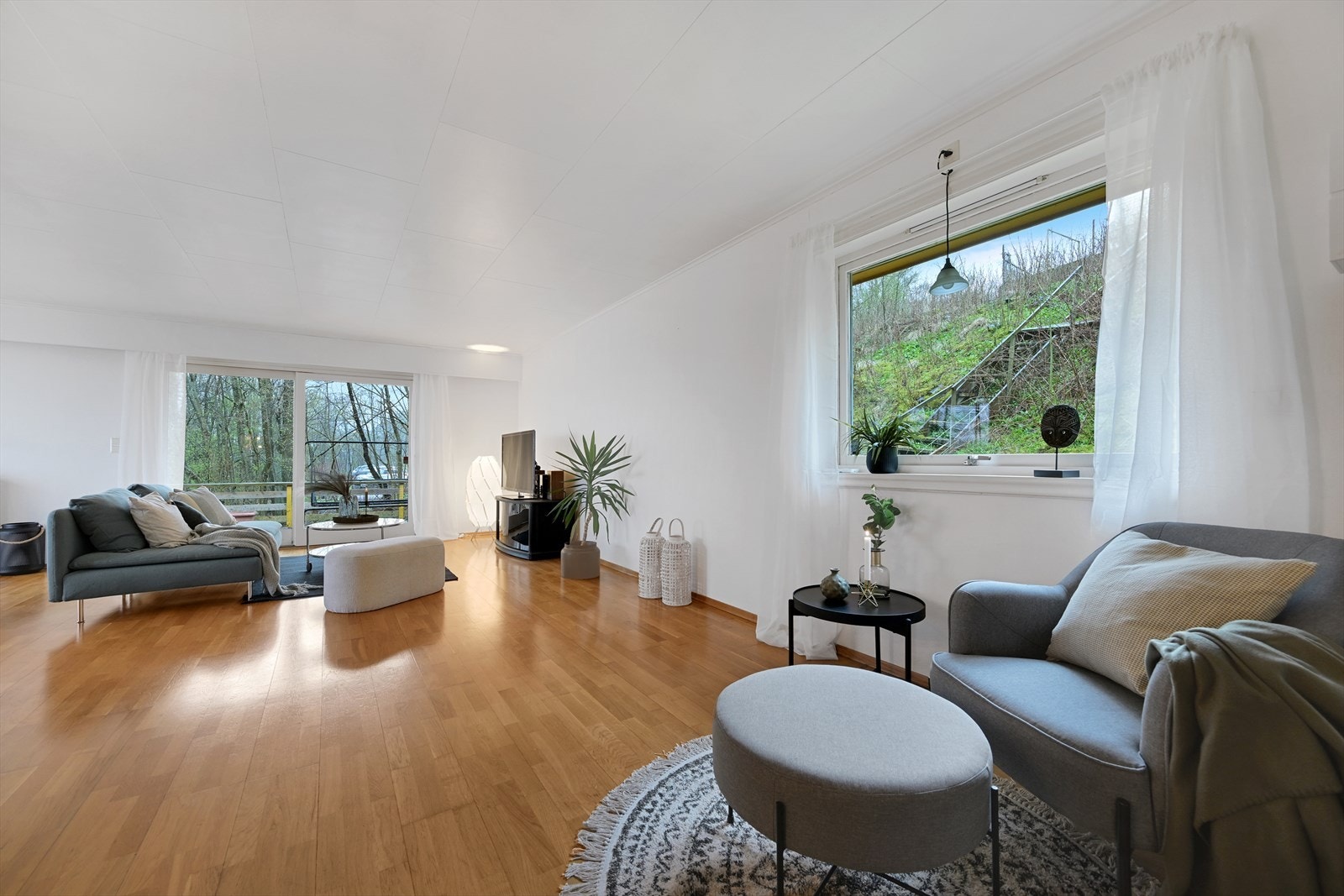 Stue sett fra trapp, med skyvedør ut til veranda rett frem, og sjøen til venstre. Galleribilde