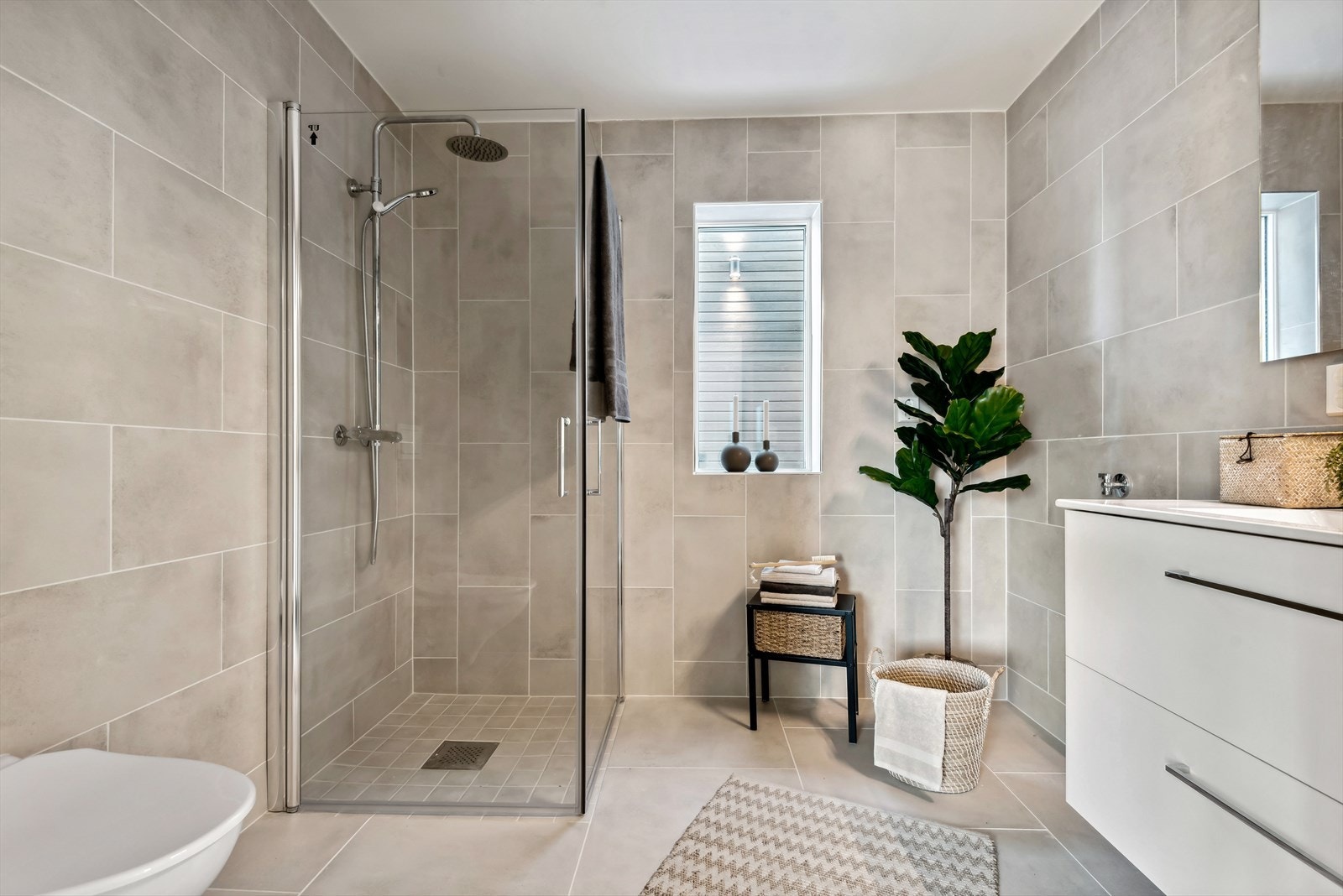 Badet har dusjhjørne, vegghengt toalett, vask med underskuffer til lagring og uttak til vaskemaskin Galleribilde