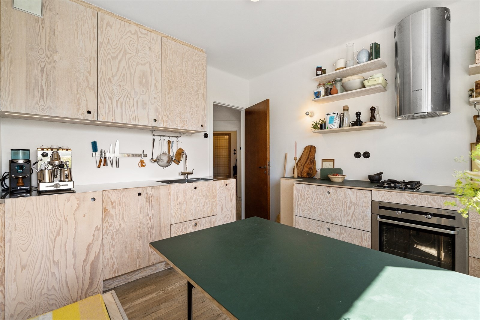Snekkerbygget innredning bestående av flotte finerfronter, rustfri benkeplate på den ene delen og benkeplate med linoleum på den andre delen. Galleribilde