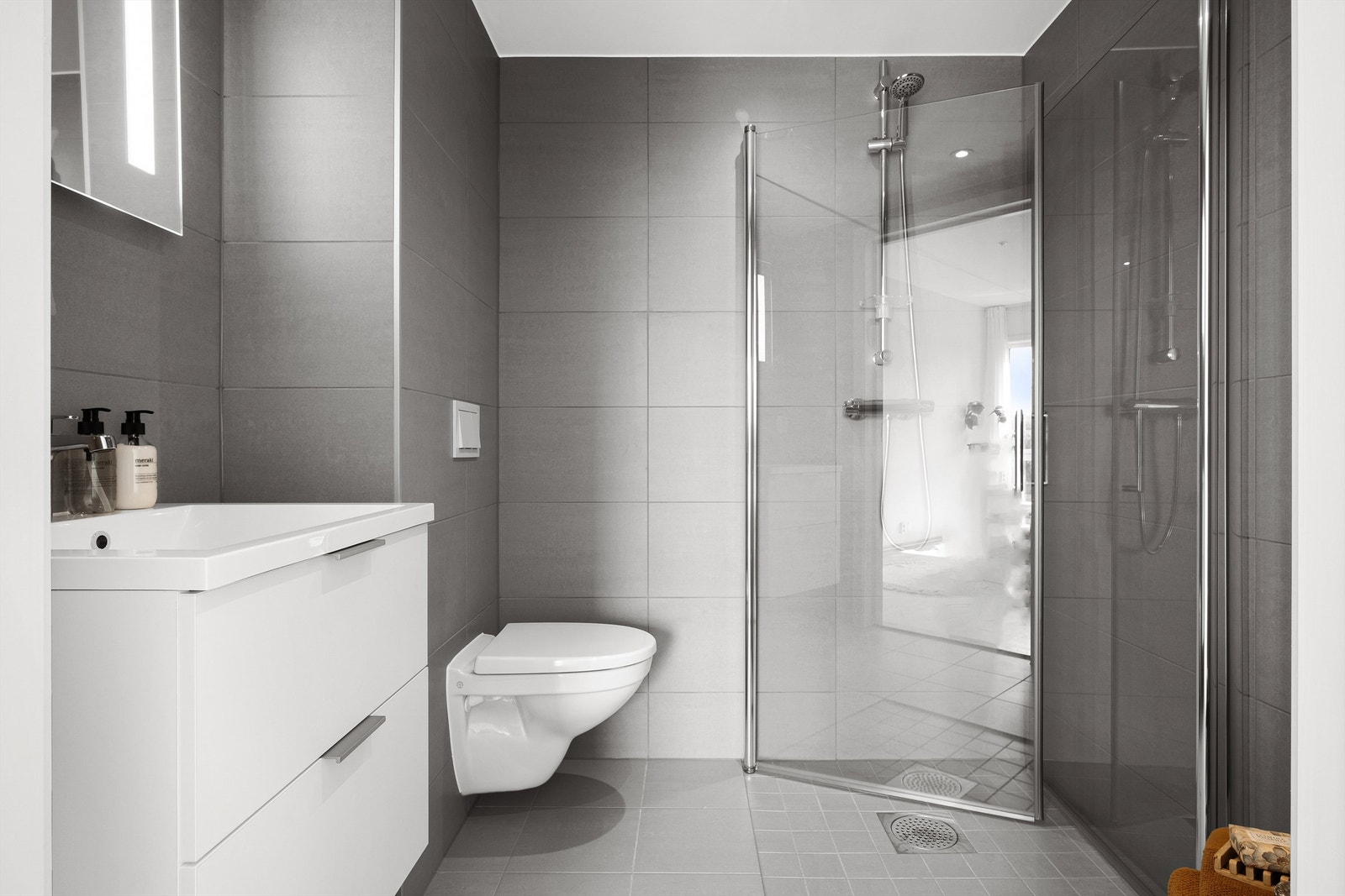 Baderommet tilknyttet hovedsoverommet er også innredet med vegghengt toalett, heldekkende servant med ettgreps blandebatteri, dusjhjørne, vegghengt speil med belysning og flislagte flater. Galleribilde