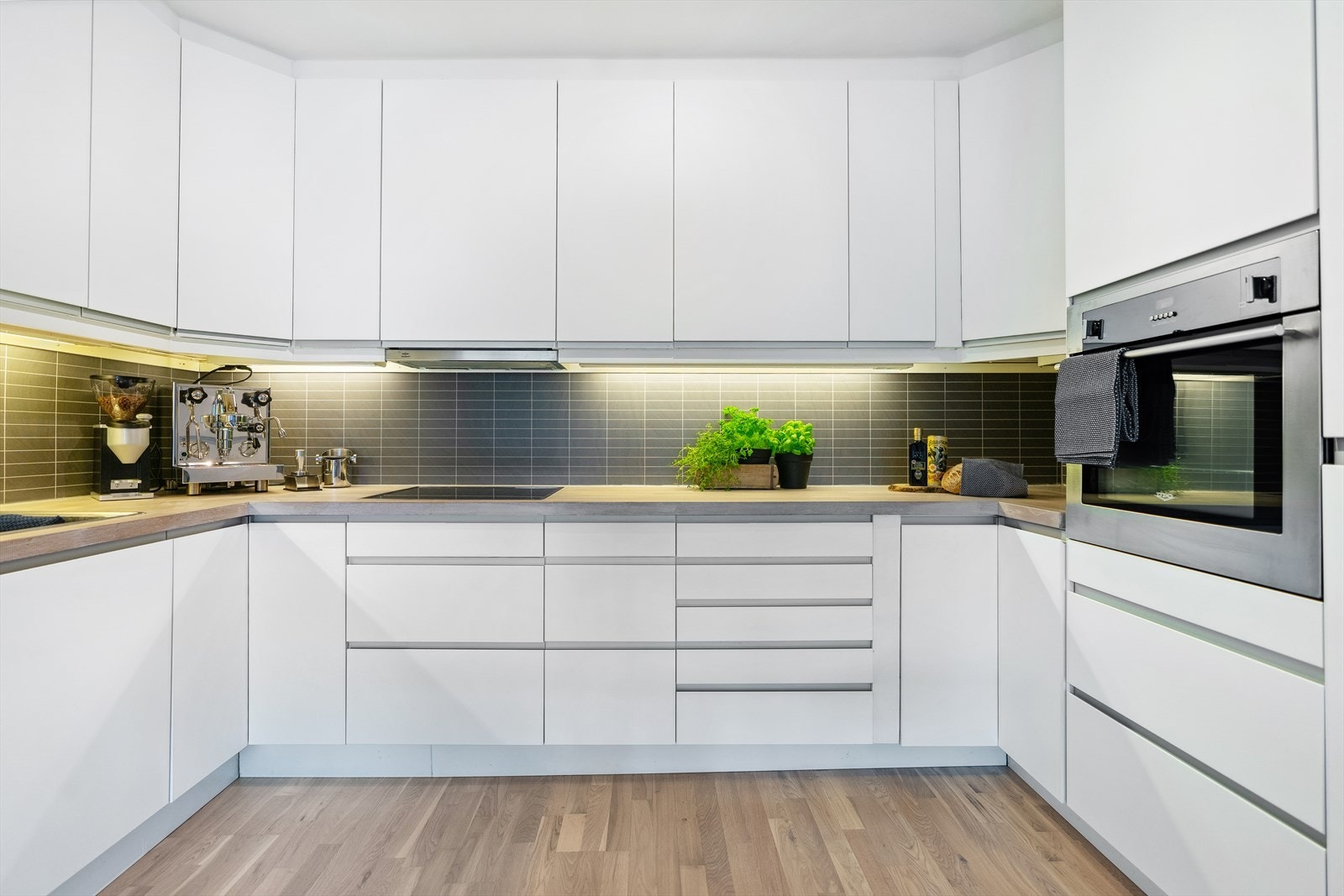 Moderne kjøkken med god skap- og benkeplass. Integrerte hvitevarer. Glatte fronter og benkeplate i heltre. Ventilator med kullfilter. Belysning og fliser mellom benk- og overskap. Galleribilde