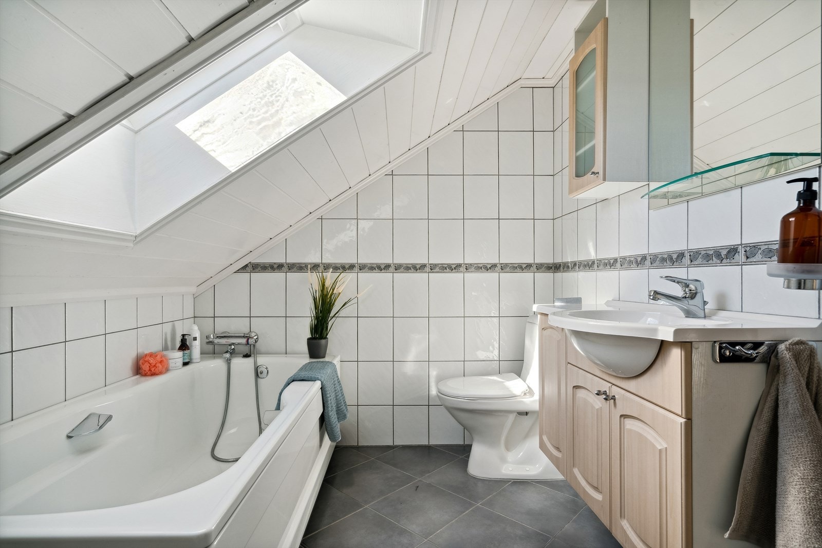 Badet i 2. etasje er innredet med servant med oppbevaring, speil, oppbevaringsskap, badekar og toalett. Galleribilde