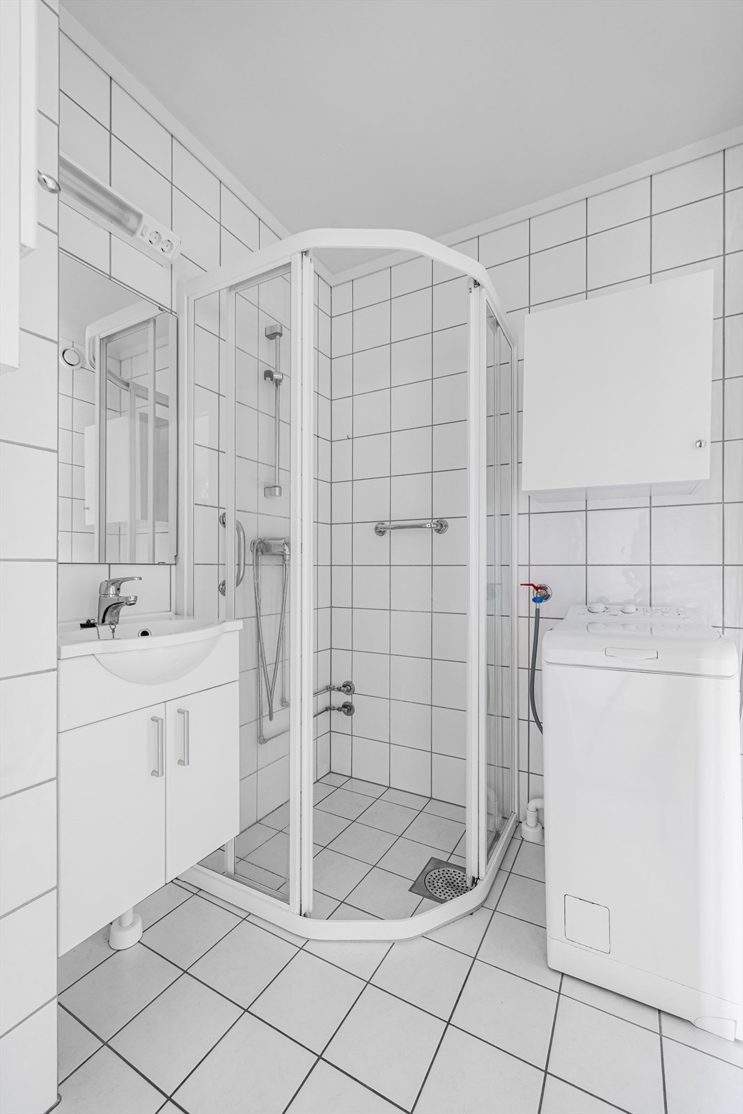 Rommet er utstyrt med en pen baderomsinnredning, dusjnisje med dusjgarnityr på vegg og glassdører foran, og opplegg og plass for vaskemaskin. Galleribilde