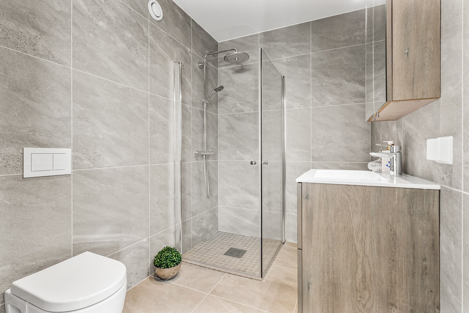 Baderomsinnredning med servant og ett-greps blandebatteri. Badet er videre utstyrt med vegghengt toalett og dusjhjørne med innfellbare glassdører. Galleribilde