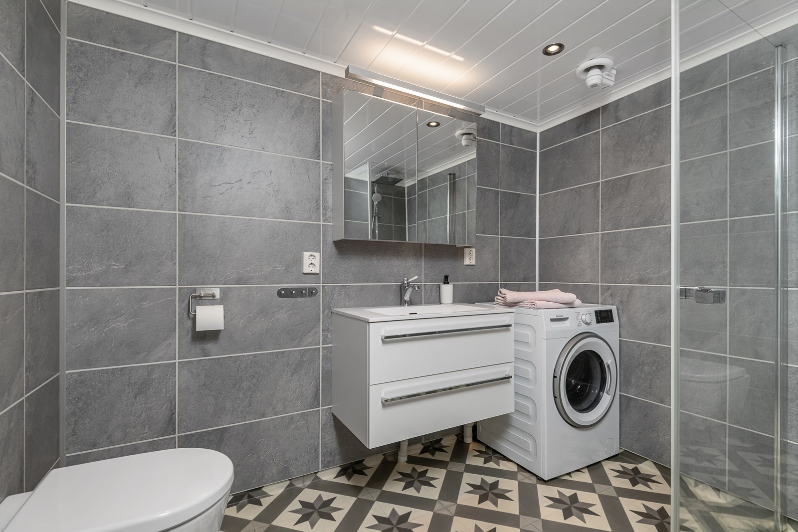 Delikat bad/wc med dusj, servantinnredning, wc og opplegg for vaskemaskin. Galleribilde