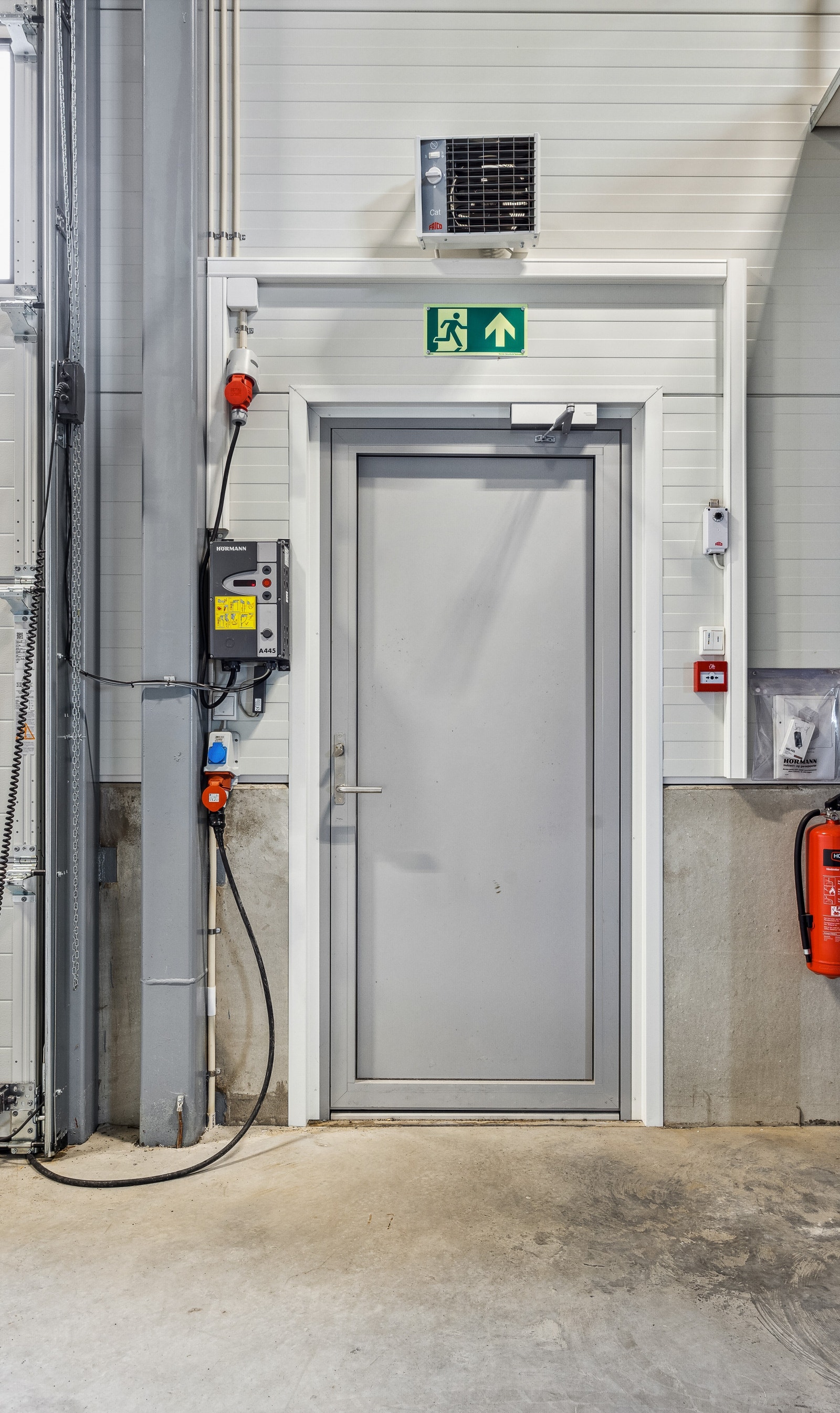 Varmeovn over dør, med brannslukkingsapparat og bryter/kontrollpanel til elektrisk leddheisport. Galleribilde