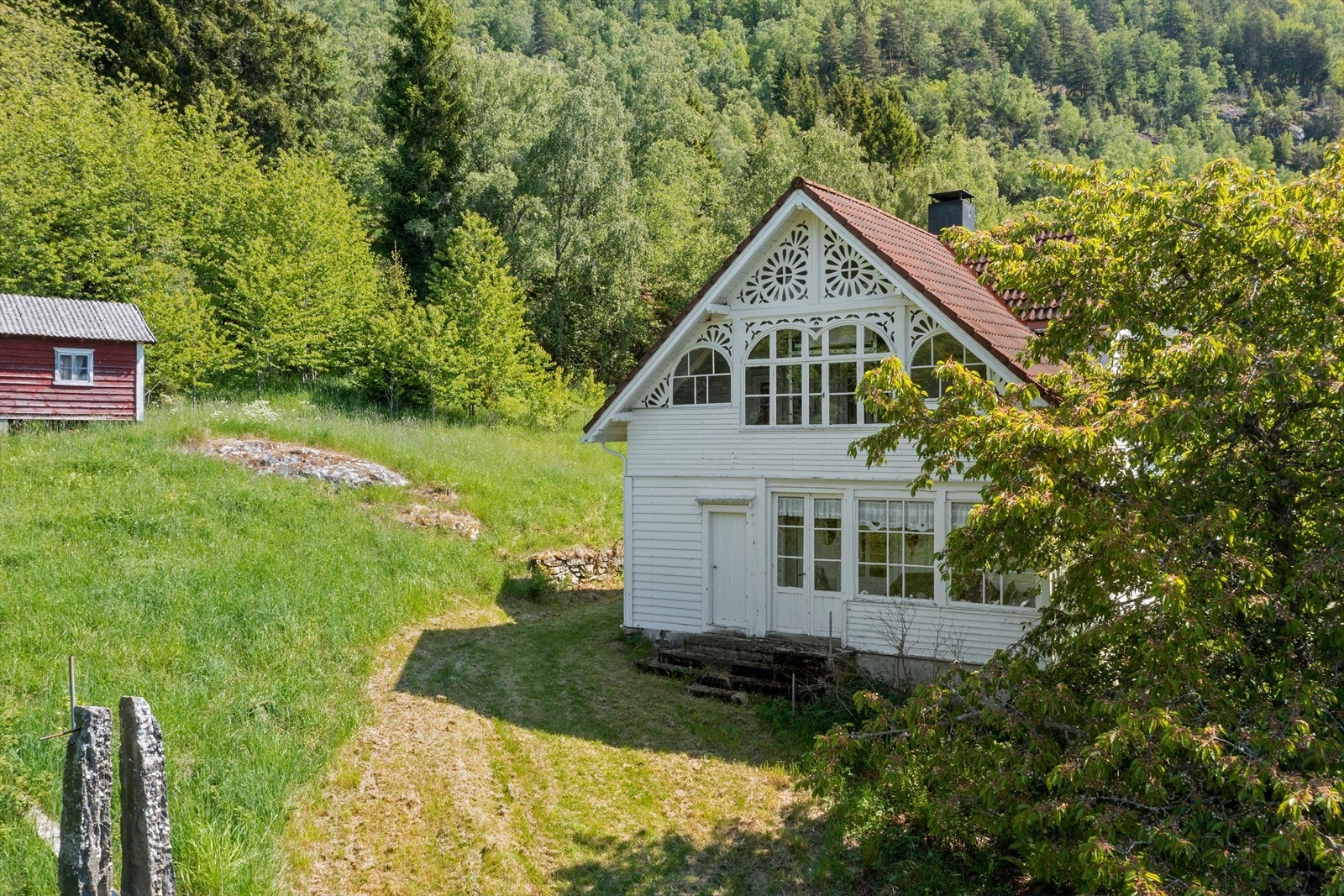Fint lite tun med diverse planter, småmurar og bergknausar, graskledde flater og skråningar. Galleribilde