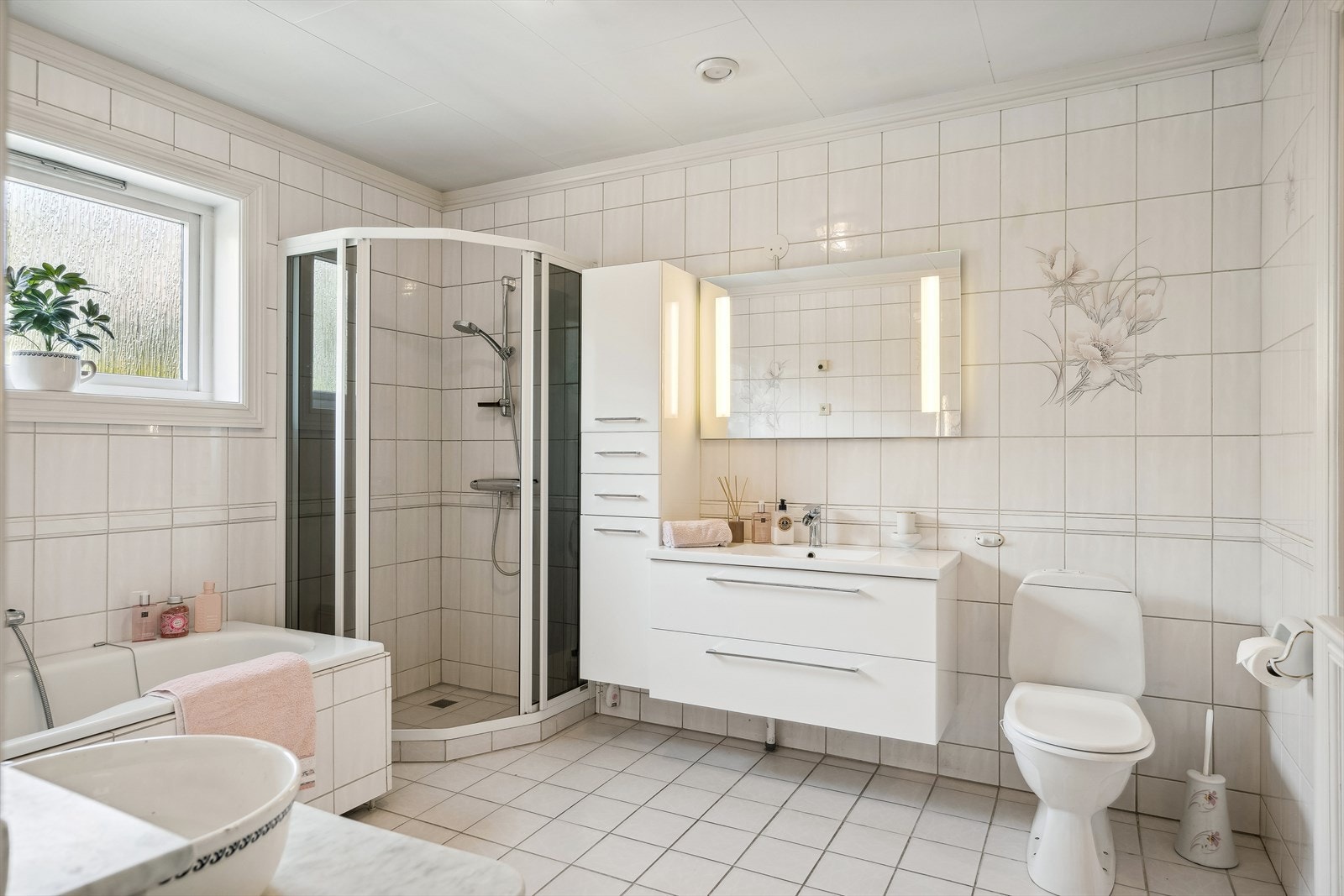 Helfliset bad med varme i gulv. Rommet er utstyrt med baderomsinnredning med glatte fronter, heldekkende servant og lysspeil på vegg. Høyskap i samme stil. Dusjhjørne, klosett, bidè og badekar. Galleribilde