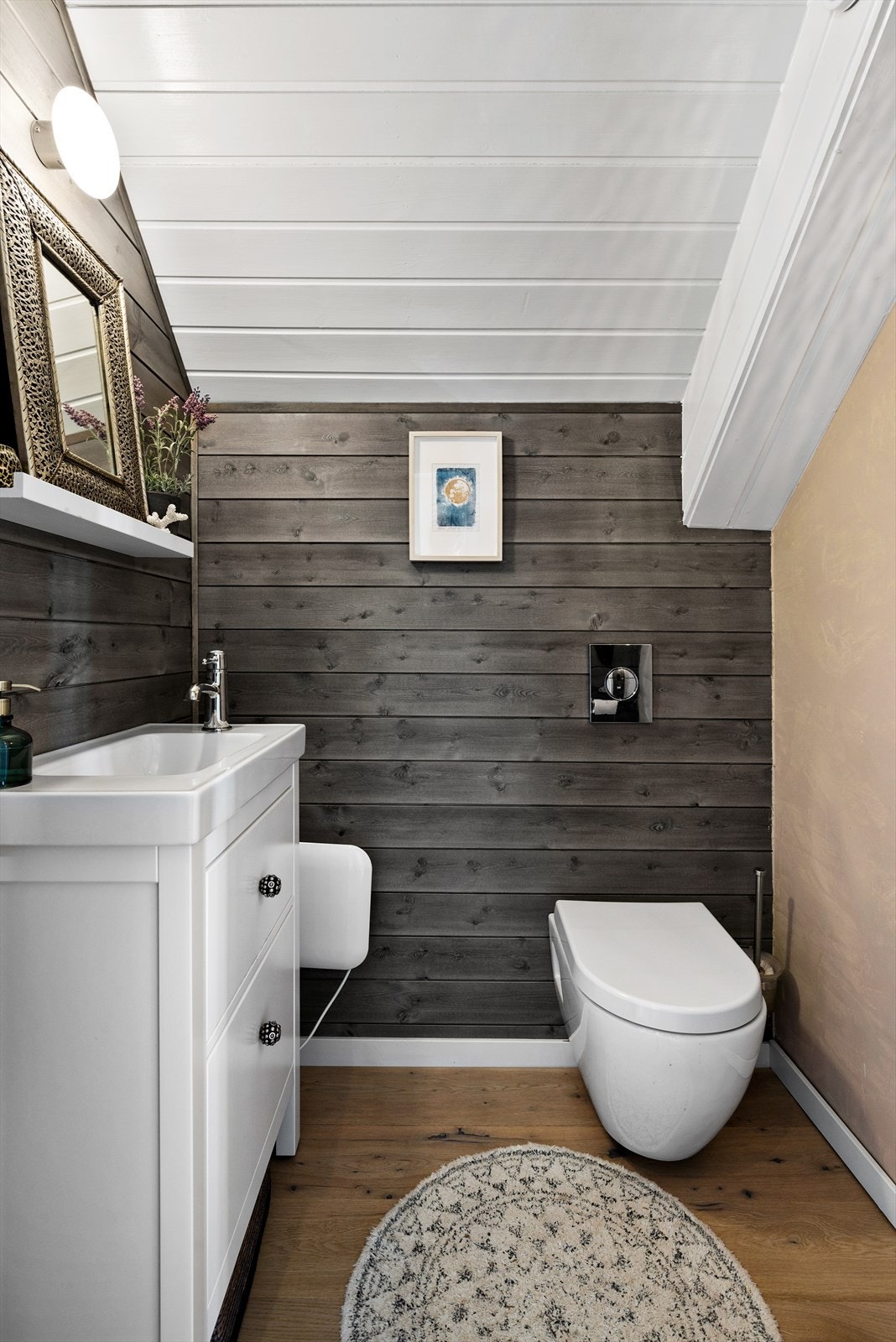 Separat toalettrom innredet med veggmontert wc, servantskap med glatte og hvitmalte fronter av tre Galleribilde