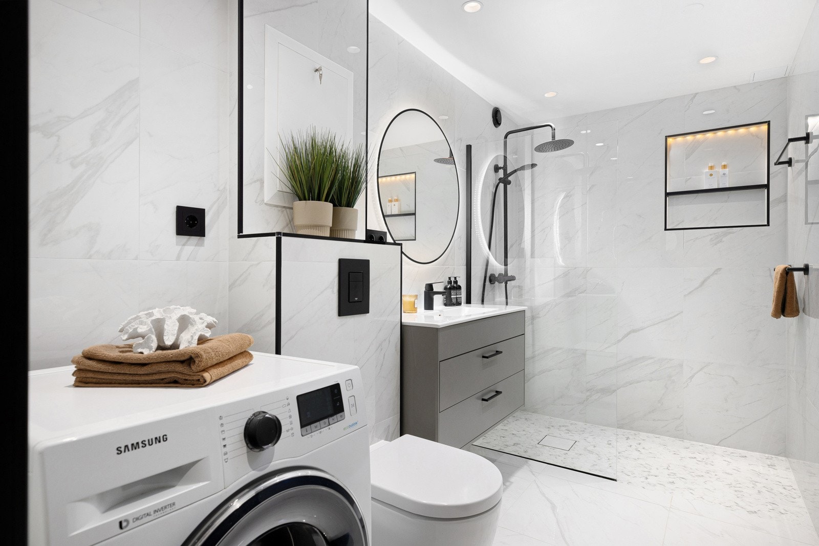 Badet i tilknytning til entréen har store og lekre gulv- og veggfliser, gulvvarme og downlights i himling. Innredningen består av helstøpt servant over benkeskap med skuffer, speil med belysning og regnfallsdusj Galleribilde