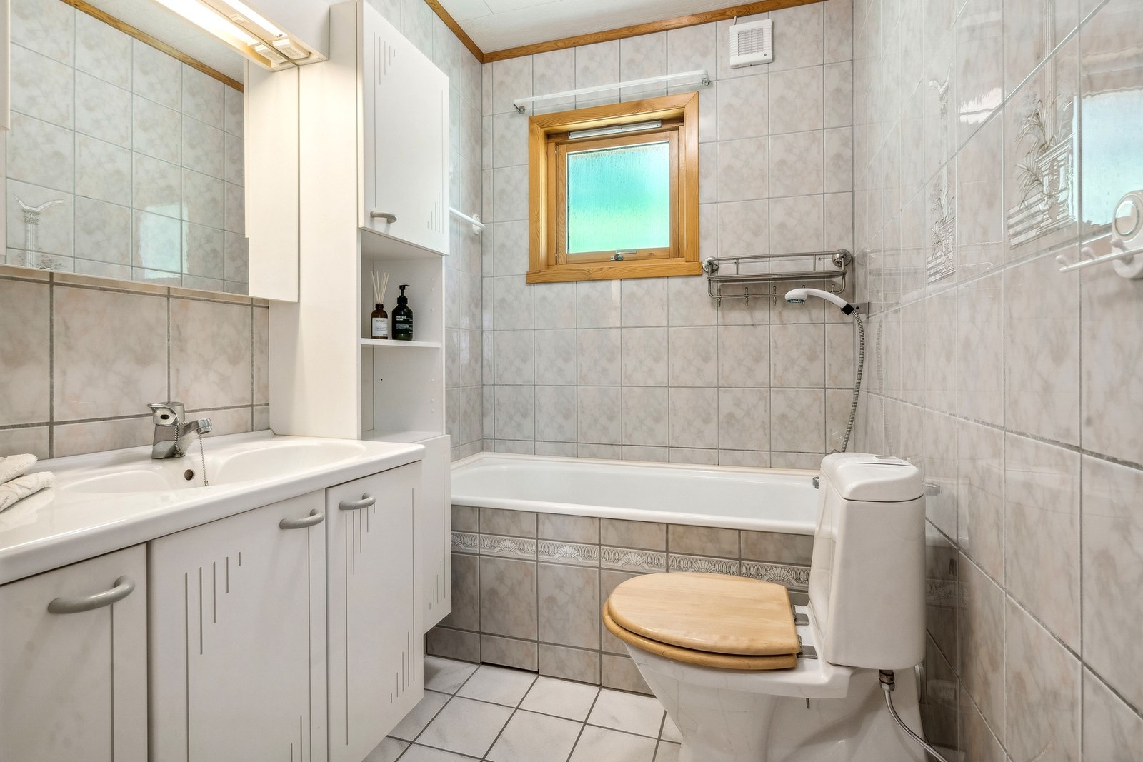 Eldre flislagt bad med toalett, badekar og baderomsinnredning Galleribilde