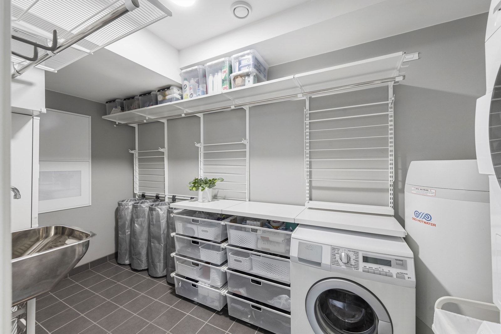 Praktisk vaskerom med gjennomtenkte løsninger. Plassbygd innredning, opplegg til to vaskemaskiner og tørketrommel. Skyllekar på vegg. Galleribilde