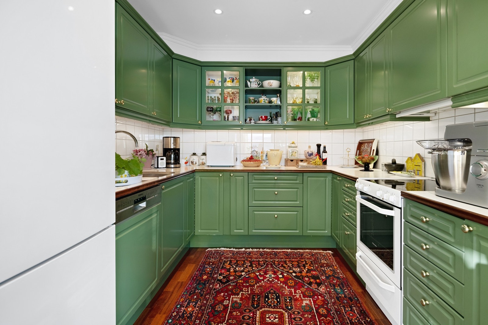 Kjøkkeninnredningen har grønne, profilerte fronter, vitrineskap, god benkeplass og hvite fliser over benken. Galleribilde