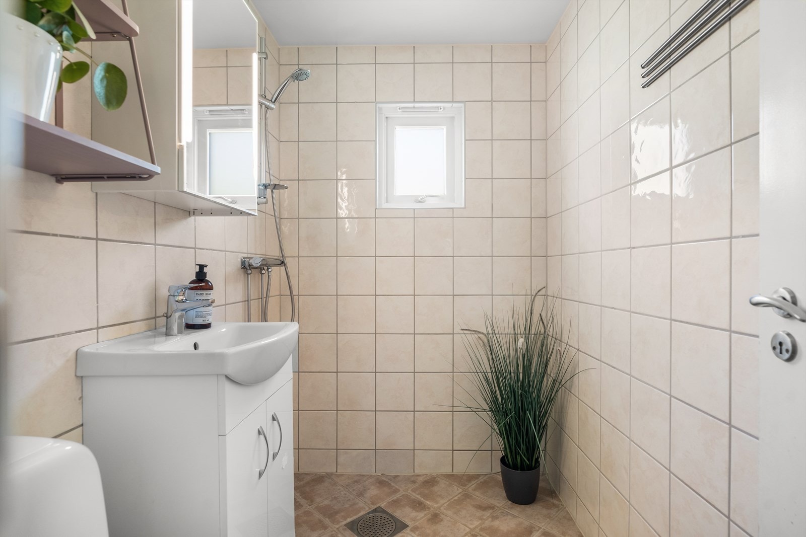 Badet har flislagt gulv med varmekabler og flislagte vegger. Det er hvit innredning med oppbevaringsplass og speilskap med integrert belysning. Galleribilde