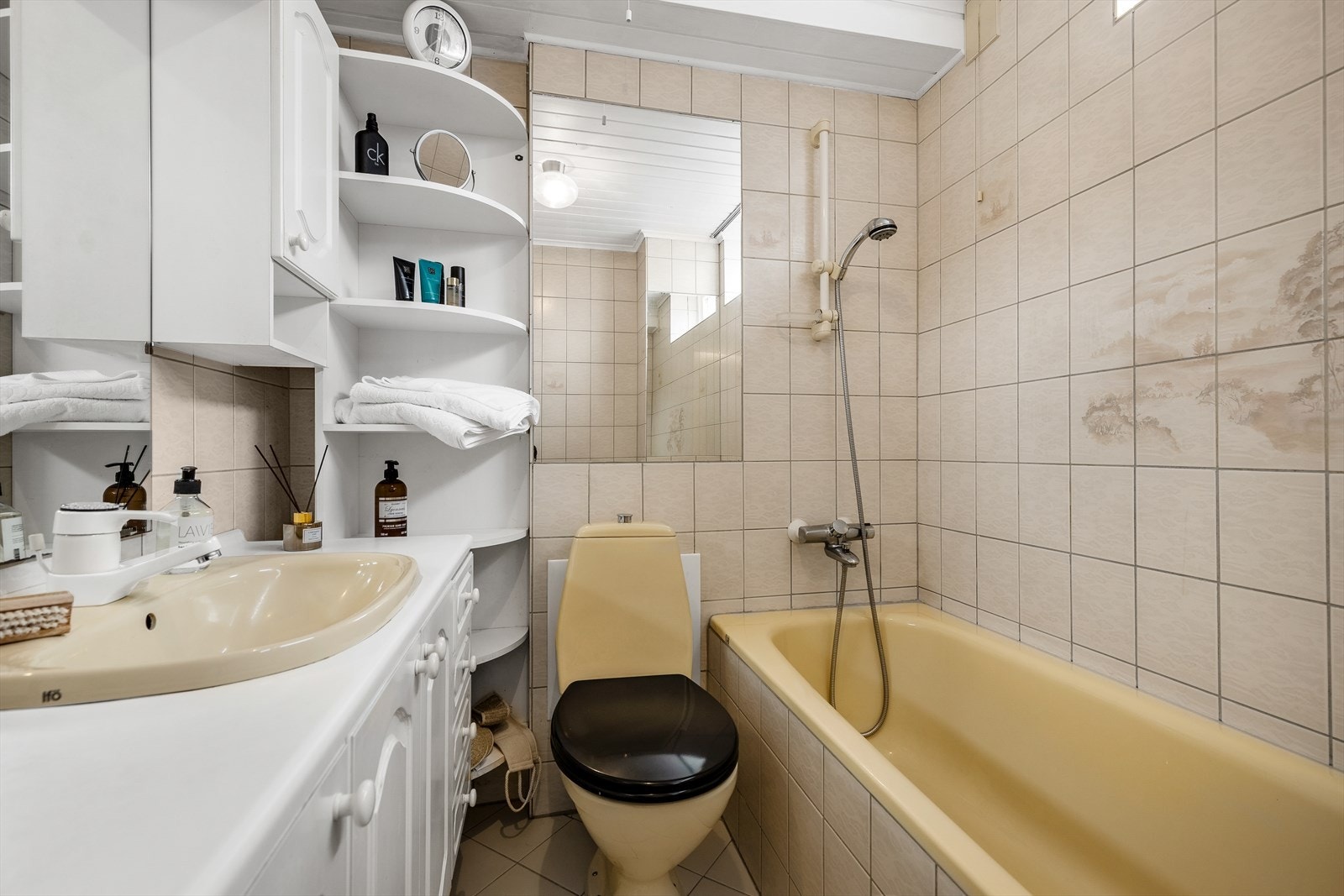 Bad innredet med toalett, badekar, servantinnredning, overskap, speil og hyller. Galleribilde