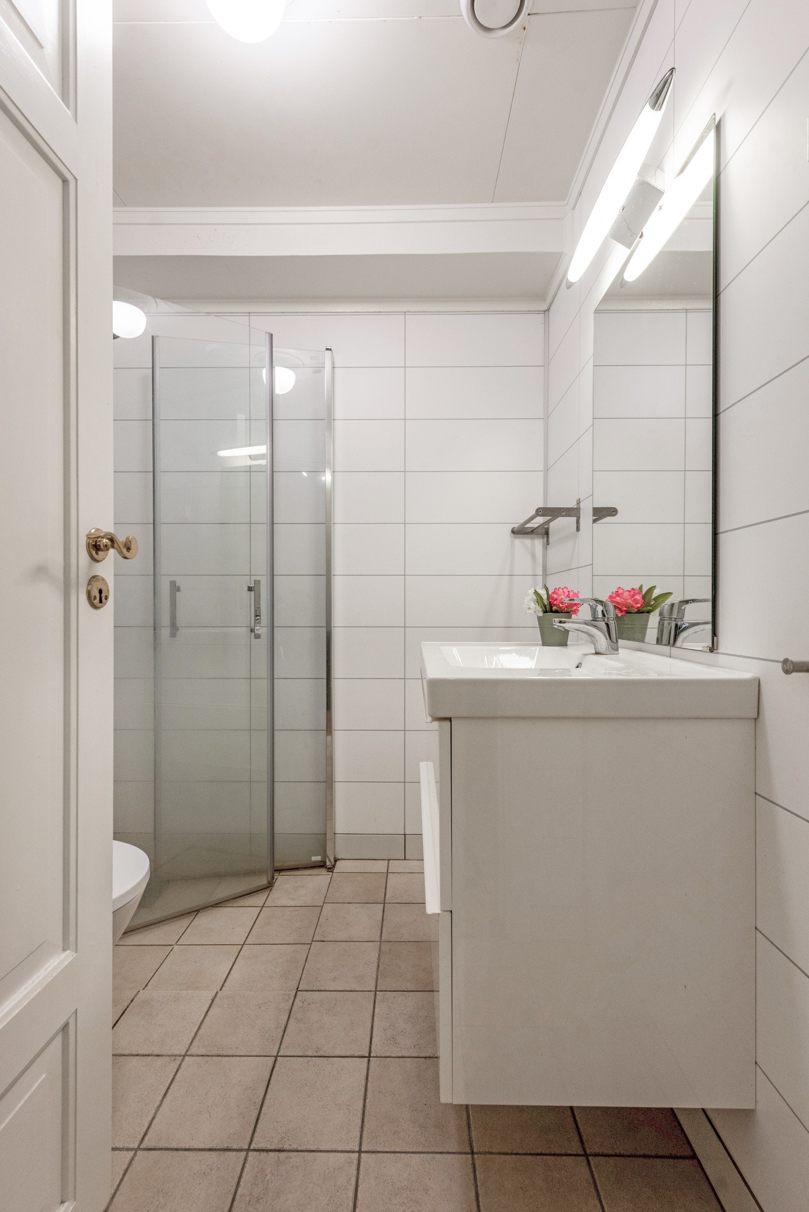 Badet er lyst og pent flislagt med baderomsinnredning, vegghengt toalett og dusjhjørne samt opplegg for vaskemaskin og tørketrommel. Galleribilde