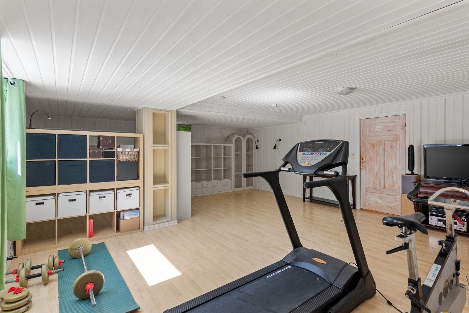 Rommet kan også fungere som trimrom og lekeplass. Gulvet har lyst laminat og veggene har lysmalte panelplater. Galleribilde