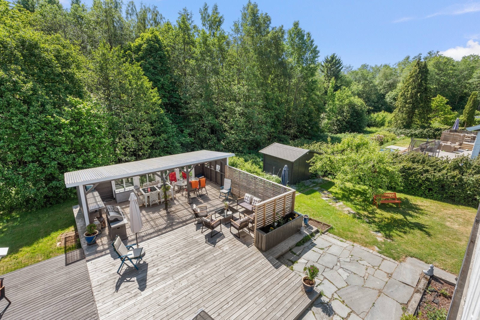 På en del av terrassen er det en høy, skjermende vegg med spiler, og en pergola/hagestue med plasttak og tre vegger. Galleribilde