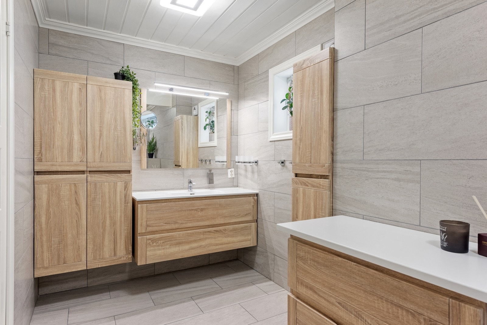 Videre har badet vegghengt toalett og en fin baderomsinnredning med folierte trefronter. Innredningen består av skuffemøblement med heldekkende servant, tre høyskap og et ekstra skuffemøblement med hvit benkeplate. Galleribilde