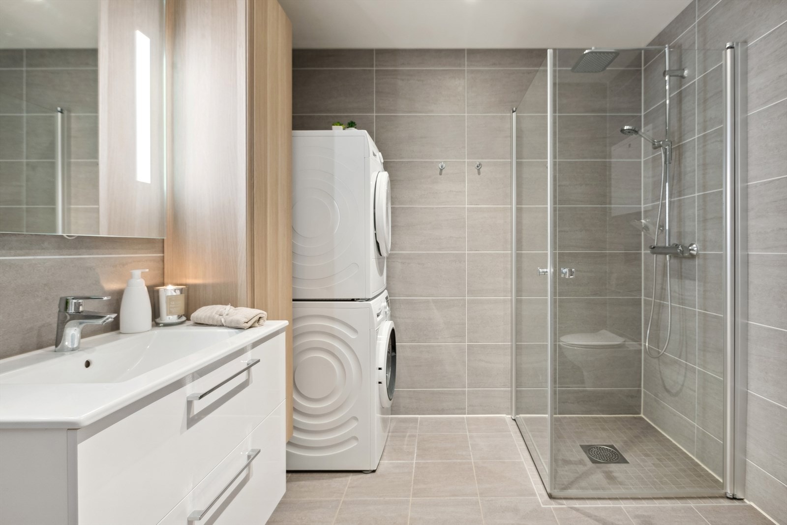 Lekkert fliselagt bad, med fliser på vegger og gulv. Badet er innredet med vegghengt toalett, baderommsinnedning og dusjhjørne med glassvegger og Watherfall dusj. Galleribilde