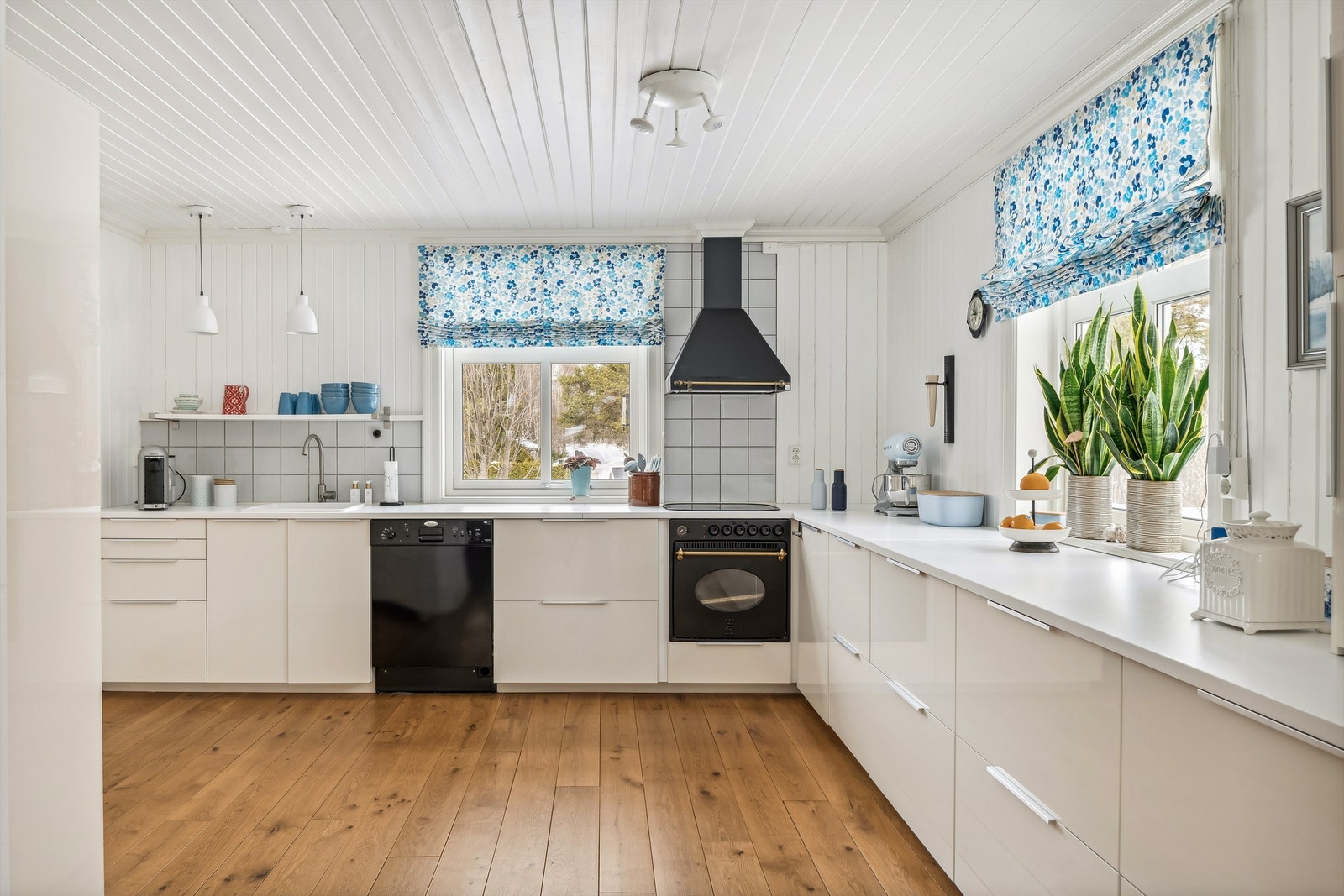 Her kan vi presentere en innredning med glatte fronter, laminat benkeplate med nedfelt kum og koketopp og integrert oppvaskmaskin. Fliser over benk. Åpen løsning mot spisestue. Galleribilde