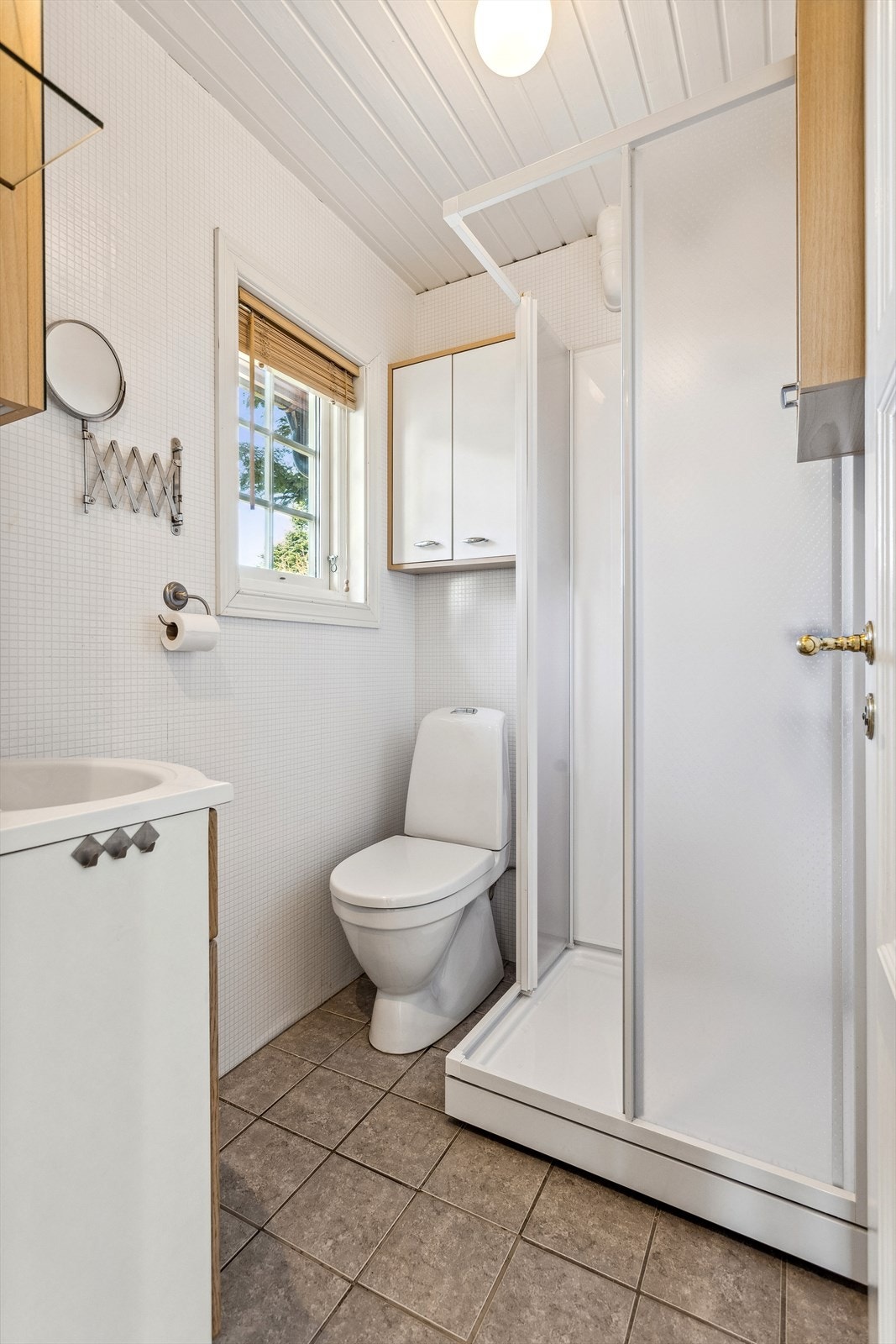 Badet har flislagt gulv (lagt oppå belegg) og er innredet med servantskap, overskap, toalett og dusjkabinett. Galleribilde