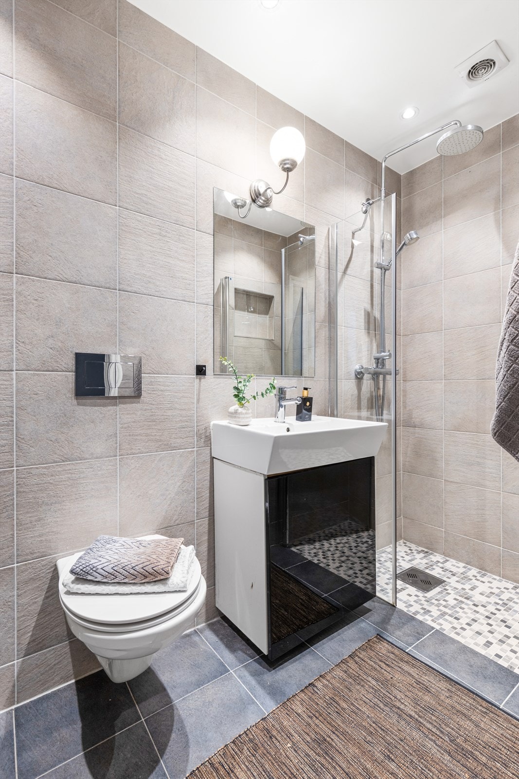 Badet er innredet med vegghengt klosett, servant nedfelt i innredning og dusjnisje med glassvegg. Galleribilde