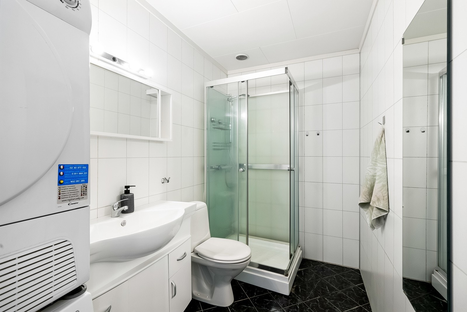 Pent bad innredet med fliser på gulv og baderomsplater på vegg. Badet er innredet med baderomsinnredning, toalett, dusjløsning og opplegg til vaskemaskin. Galleribilde